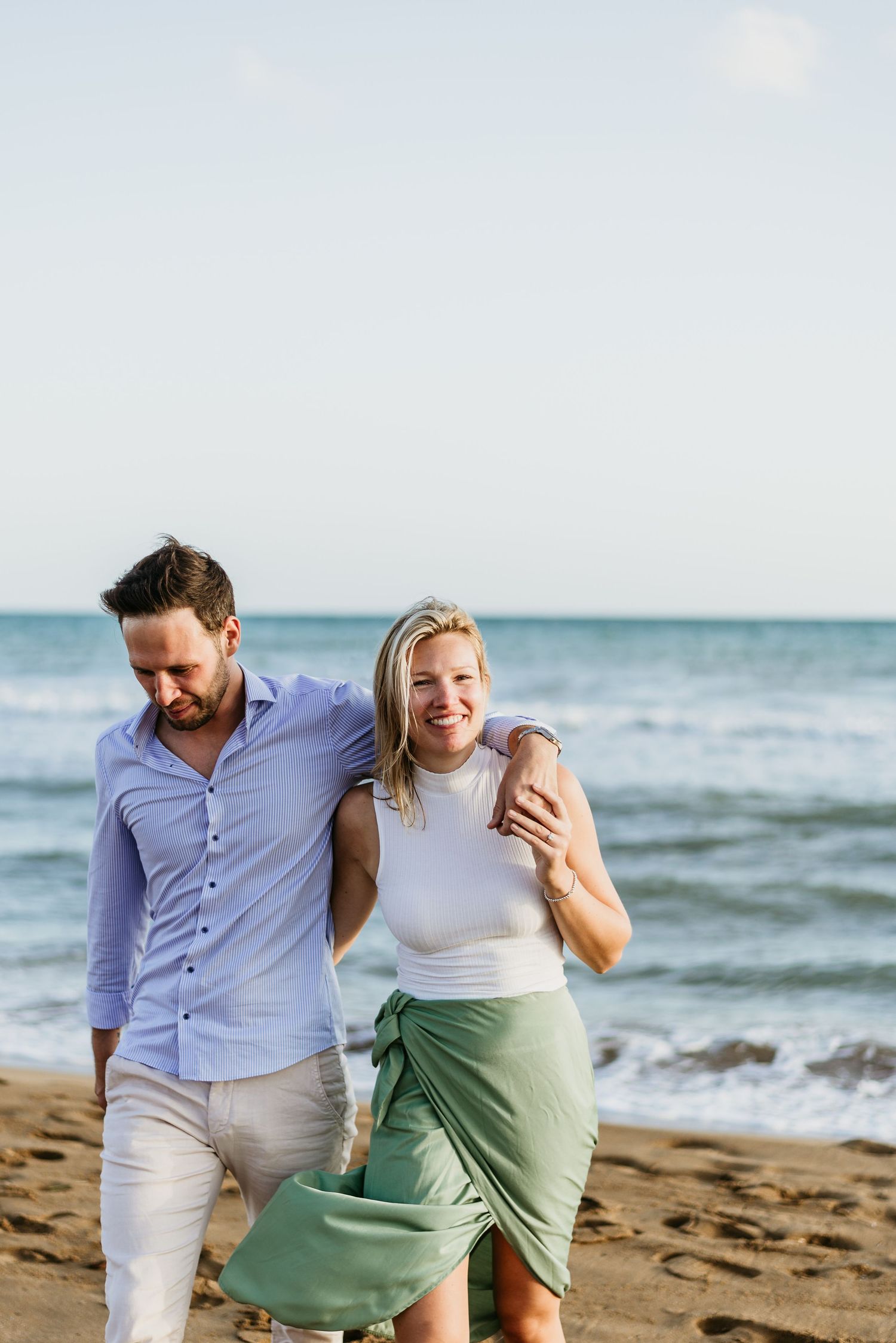 A joyful couple embraces while walking along a sandy beach with ocean waves in the background.