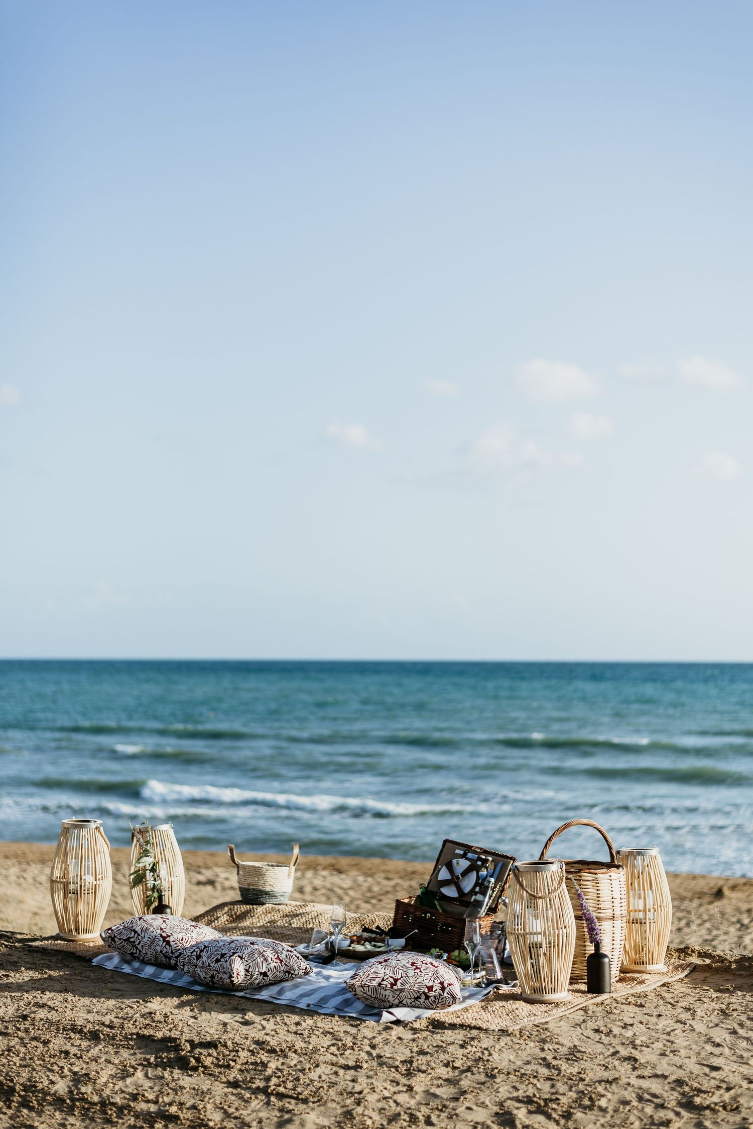 Beachside picnic setup with champagne glasses and wicker basket against ocean backdrop.