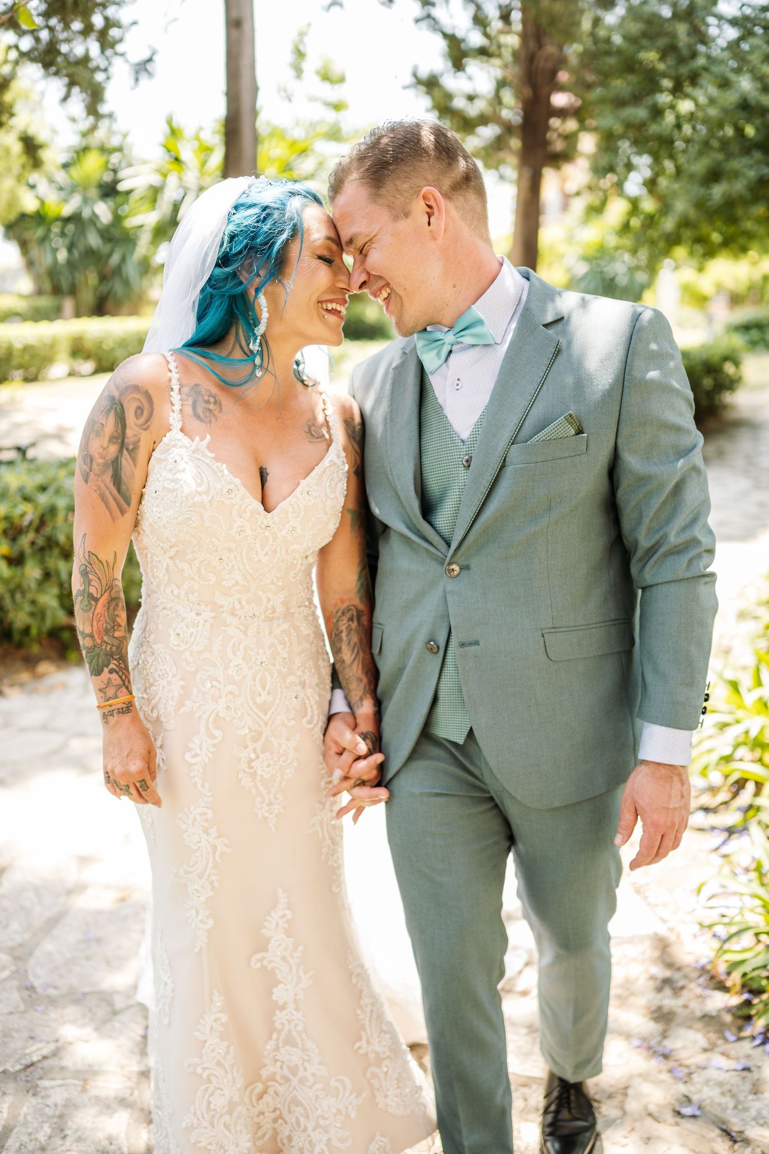 Bride in lace dress and groom in sage suit share intimate moments in a garden setting.