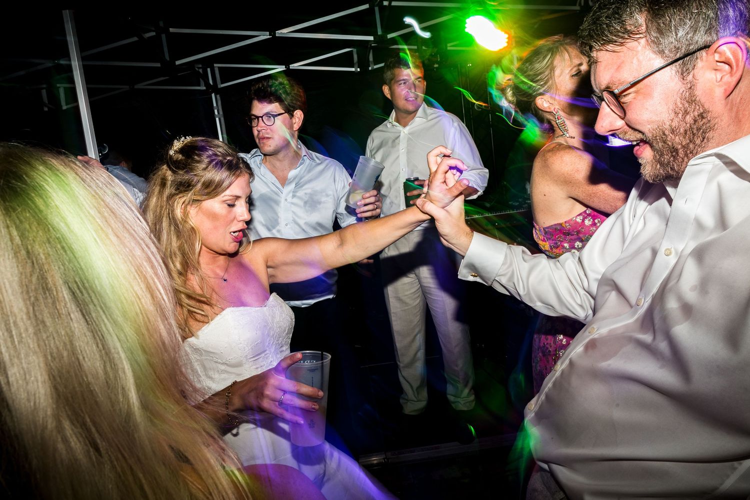 Dancers moving to music under green and purple lighting at an indoor celebration.