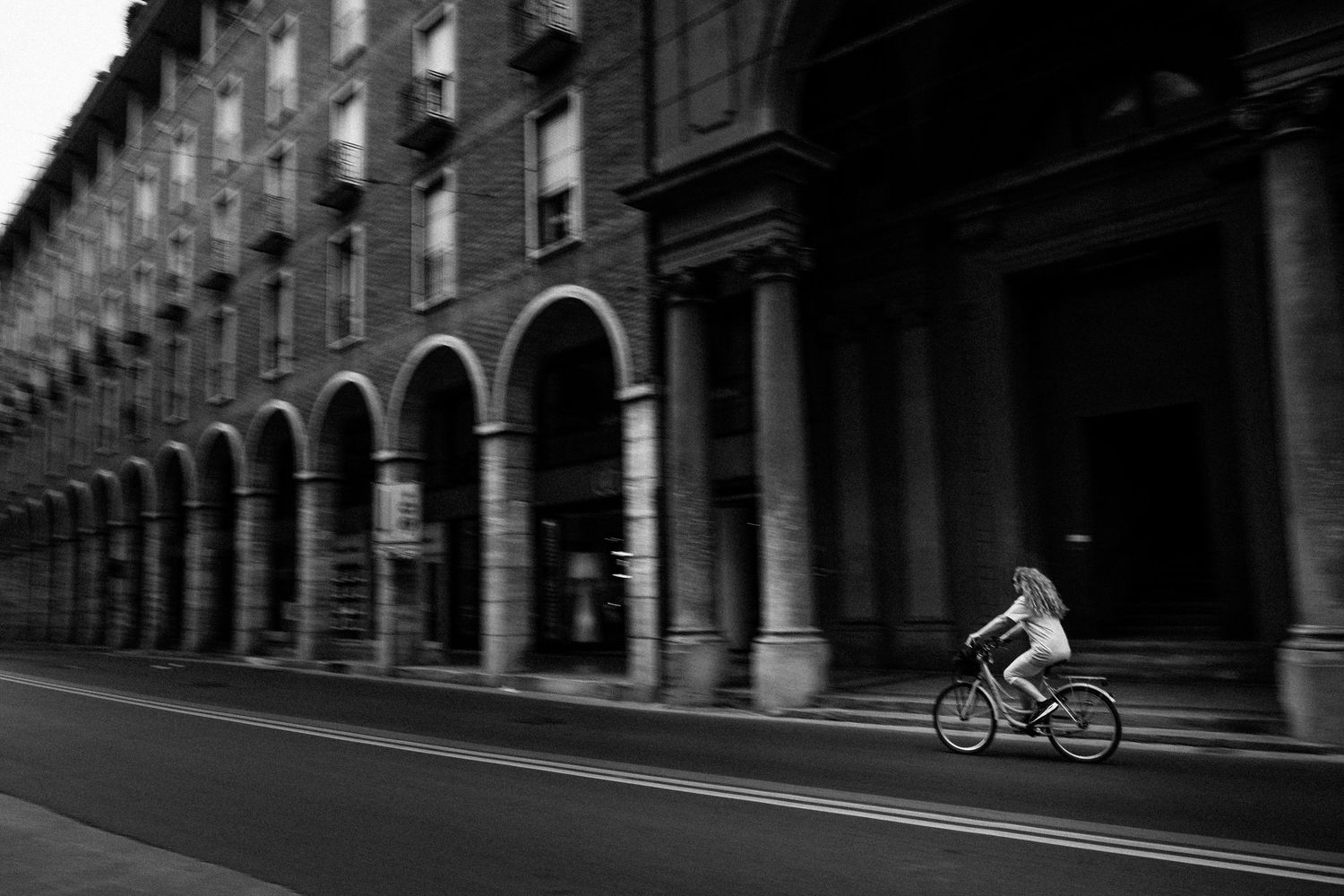 Cyclists riding along a street lined with historic buildings and arched architecture.
