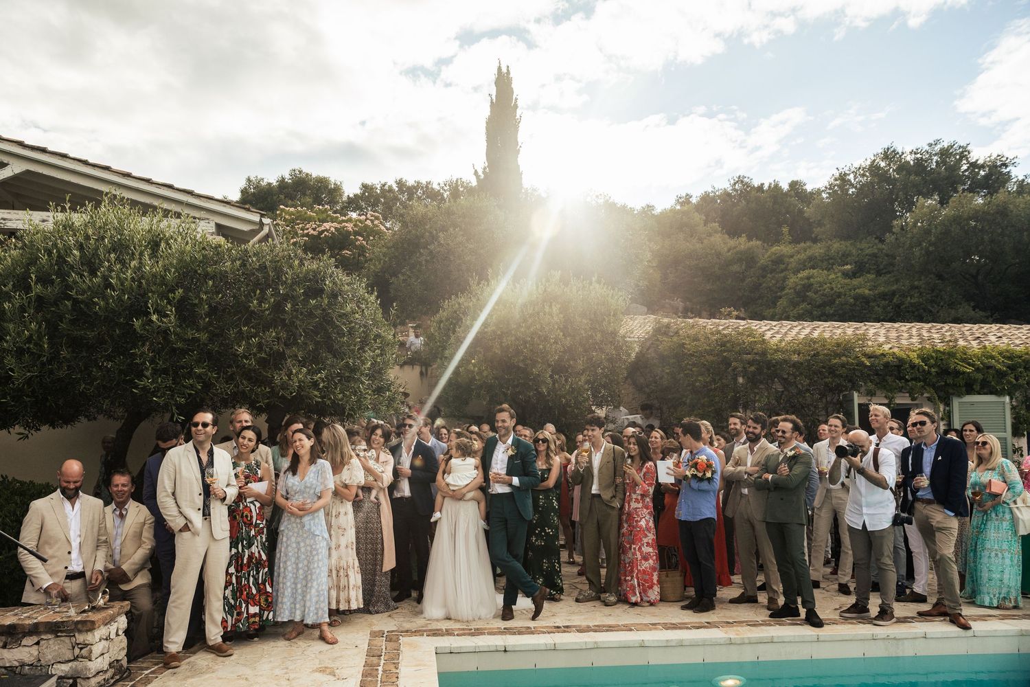 Large wedding party group photo by a pool with mountain scenery in the background.