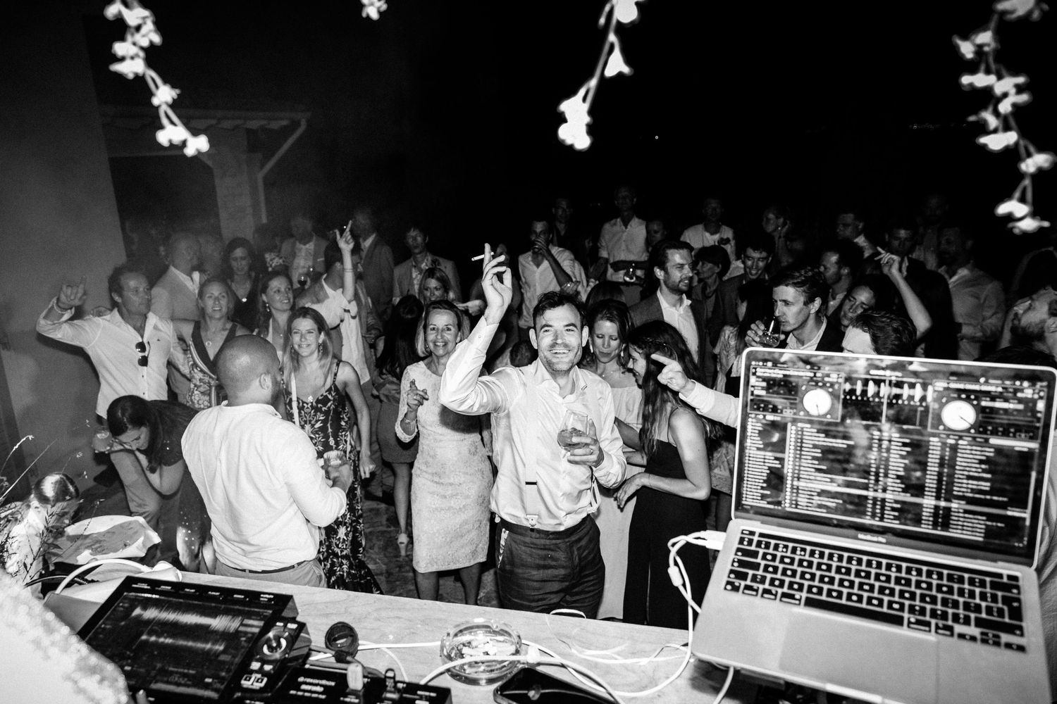 Crowded dance floor with party guests dancing under decorative white lights.