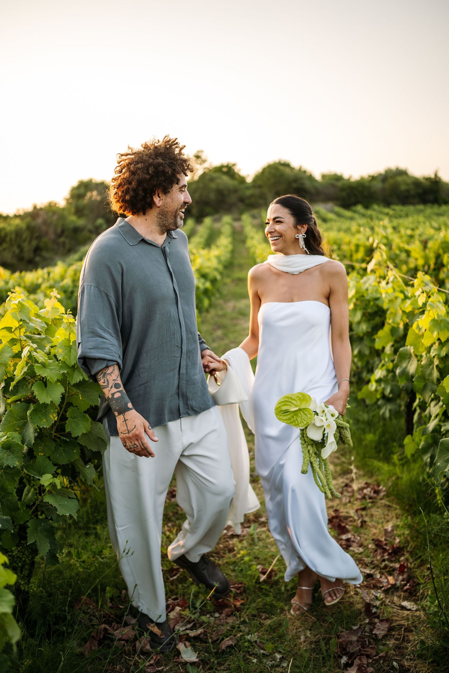 Couple sharing a joyful moment while walking through grapevines at golden hour.