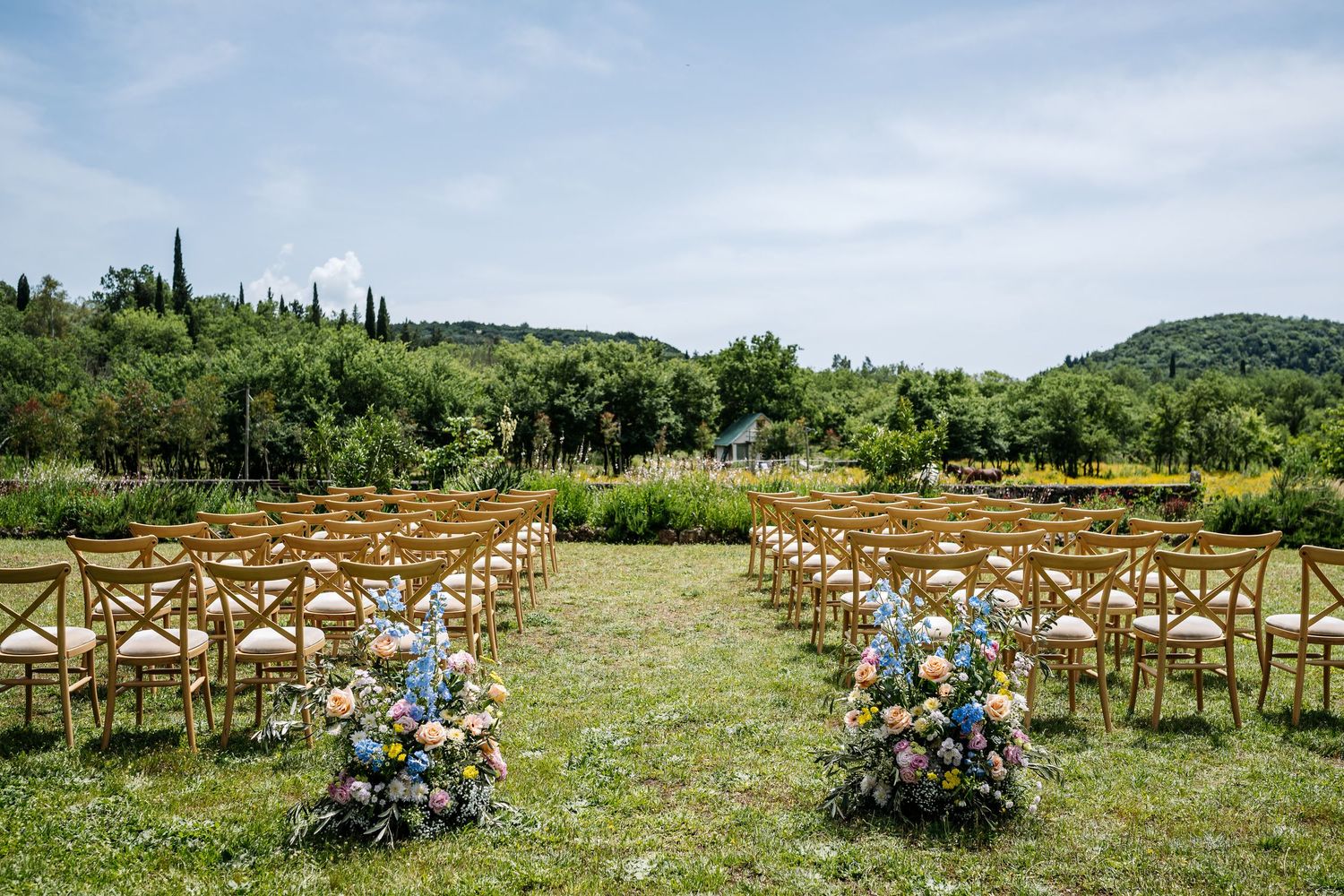 Rustic outdoor wedding ceremony setup with wooden chairs arranged in rows on a grassy hillside.