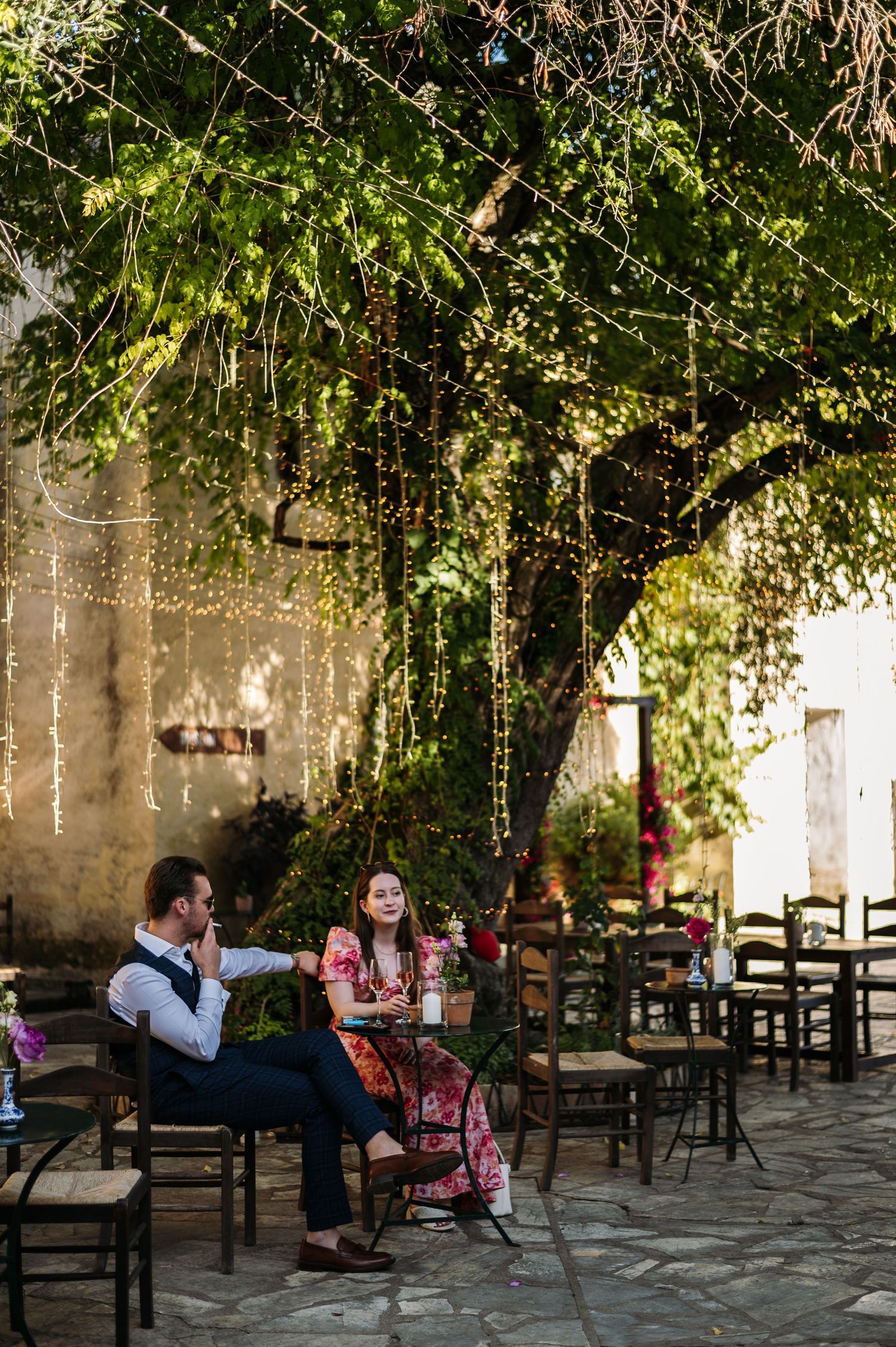 Outdoor dining area set under green trees with wooden tables and chairs.