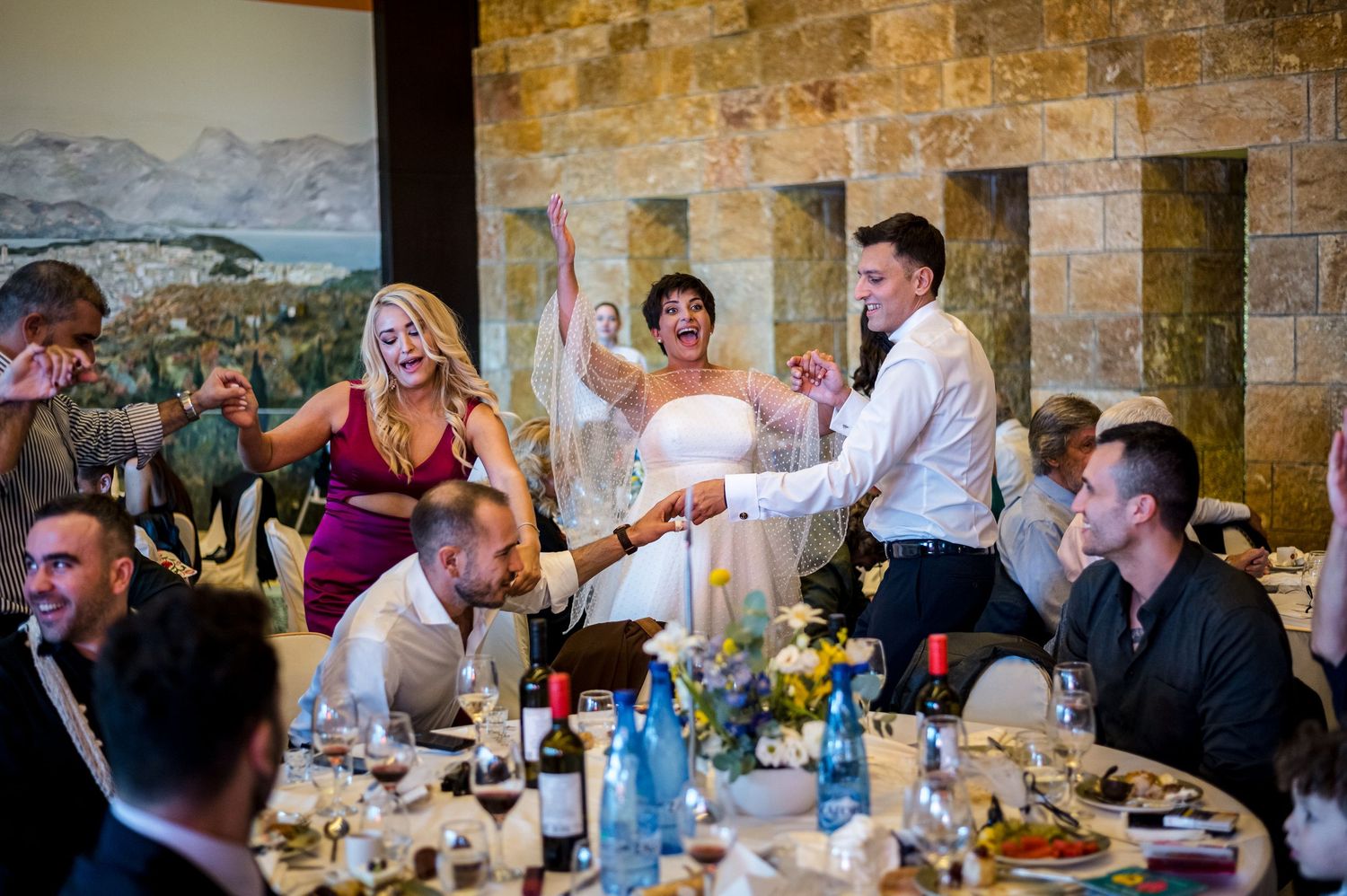 Wedding reception guests dining and socializing at rustic stone-walled venue.