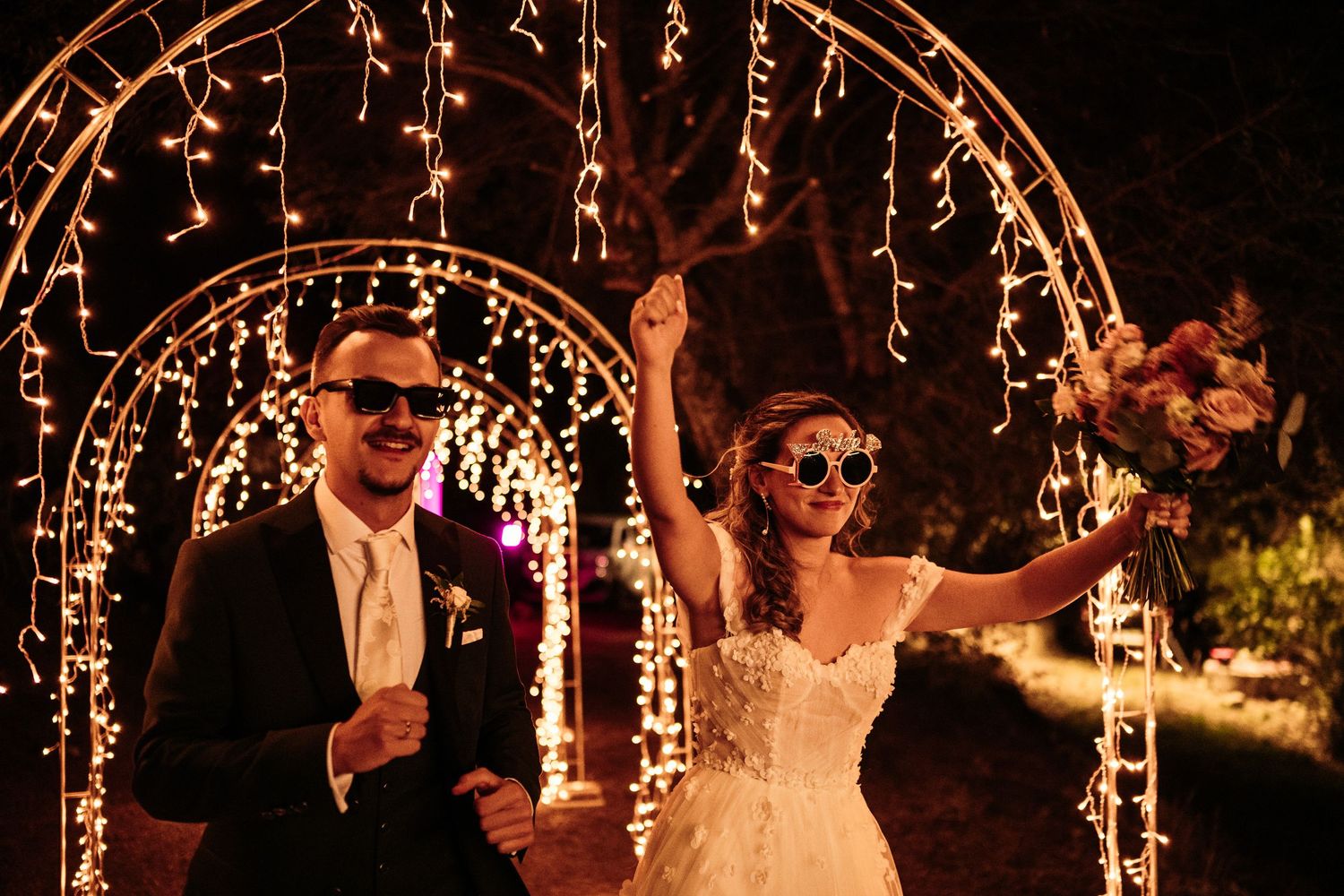 Wedding reception dance floor under twinkling fairy light arches at night.