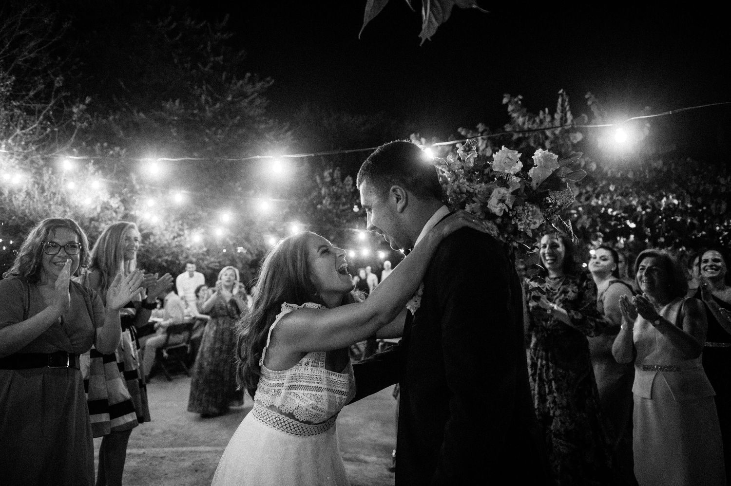 Wedding guests dance and celebrate on the dance floor under glowing lights at an evening reception.