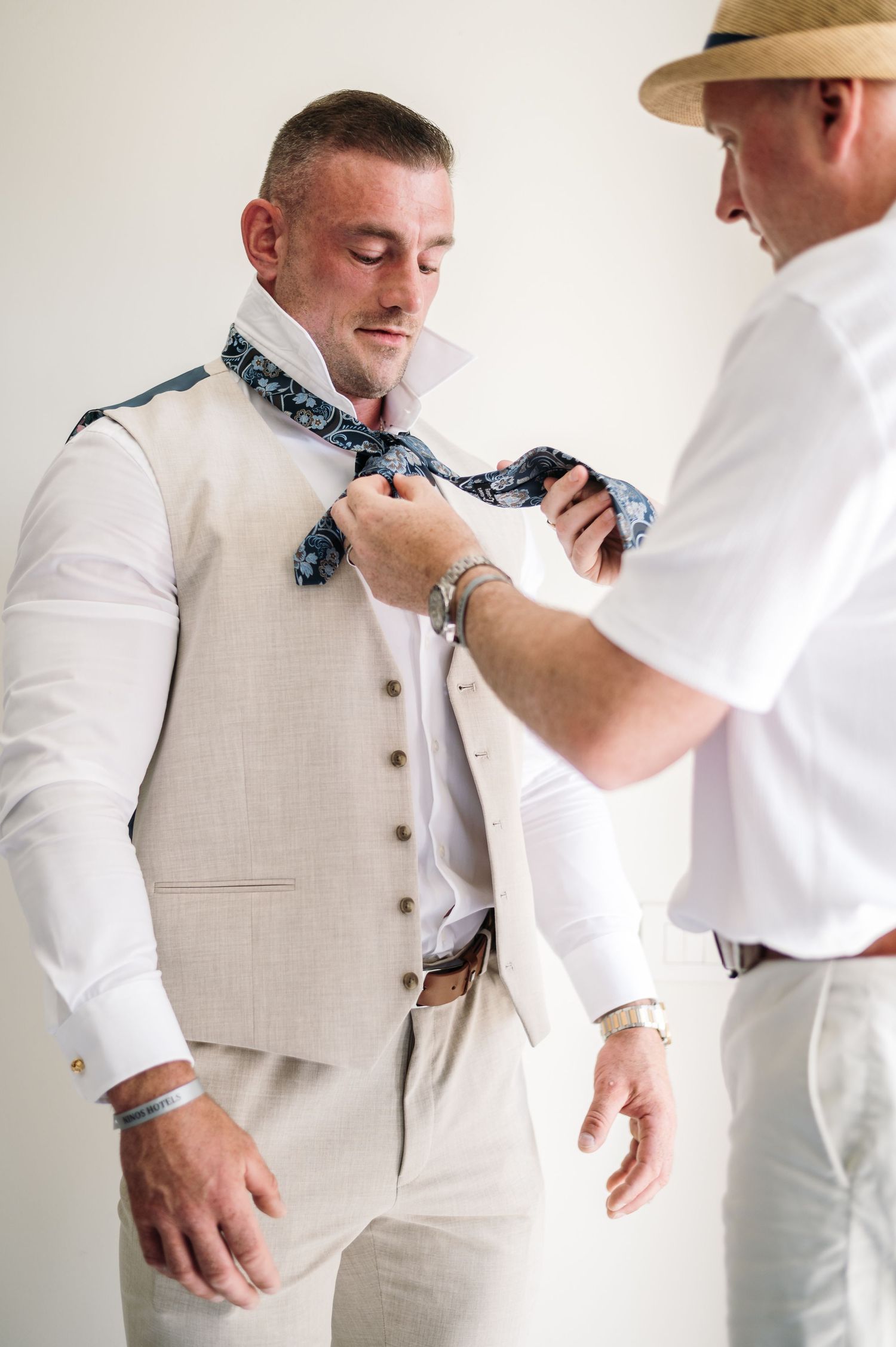 Wedding preparation scene showing the adjustment of a patterned bow tie with a light gray vest.