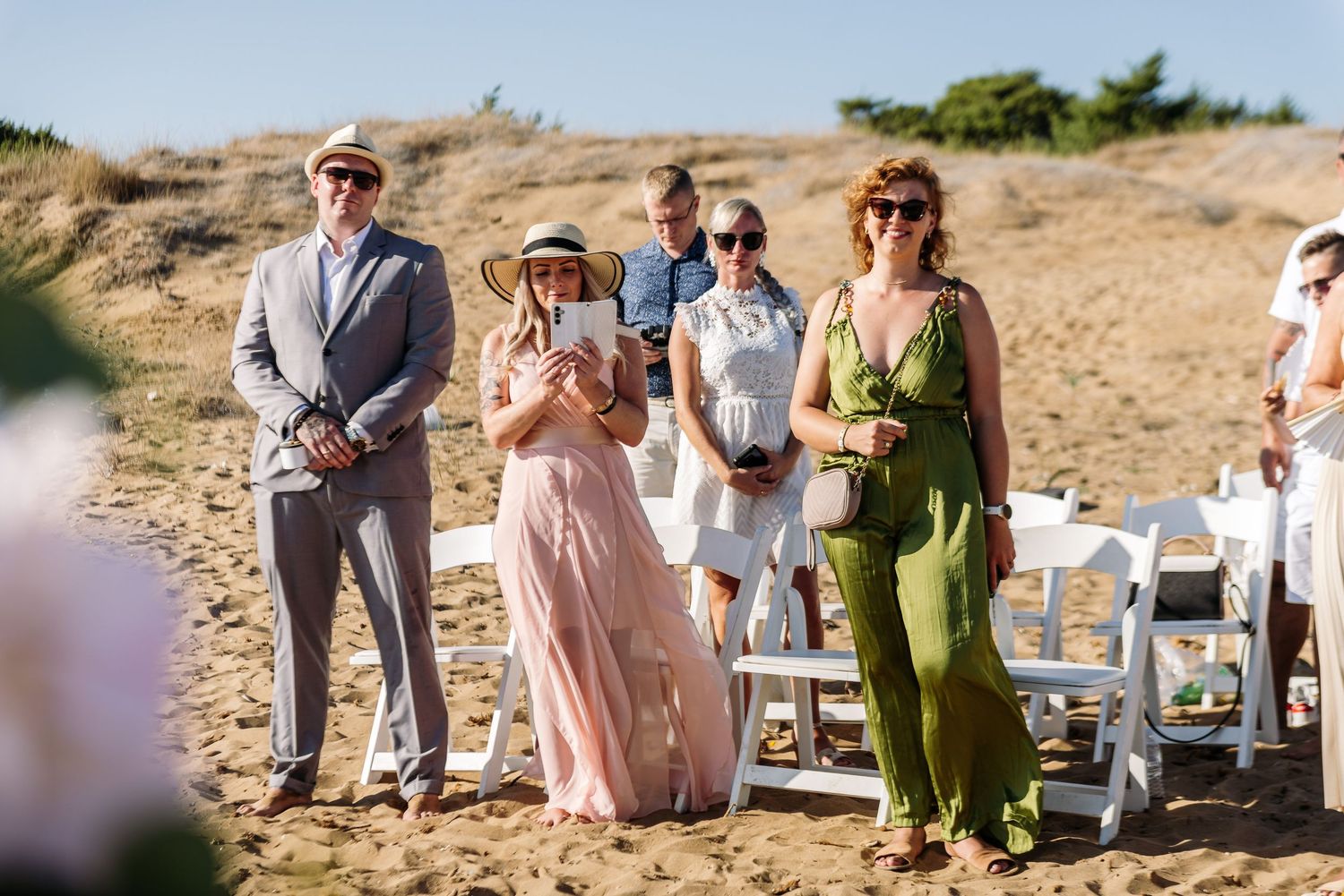 Beach wedding ceremony setup with guests seated on white chairs against coastal backdrop.