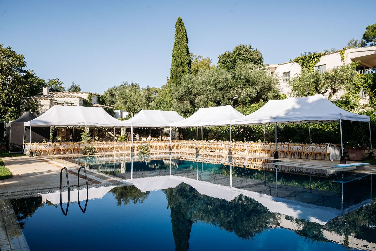 Panoramic view of a luxurious swimming pool surrounded by white umbrellas and lounge chairs in a resort setting.