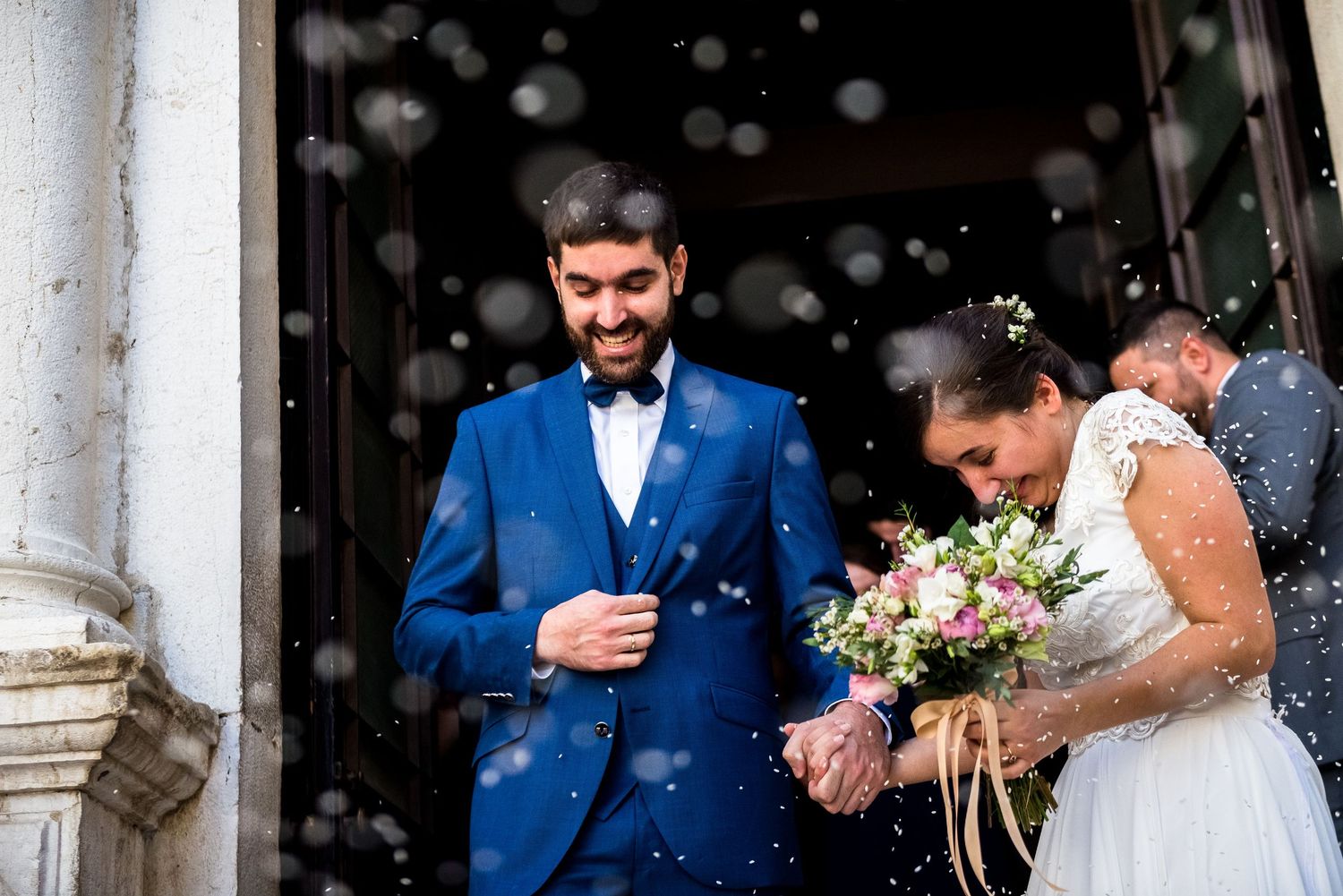 Wedding party celebration with confetti and blue suits outside a classical building.