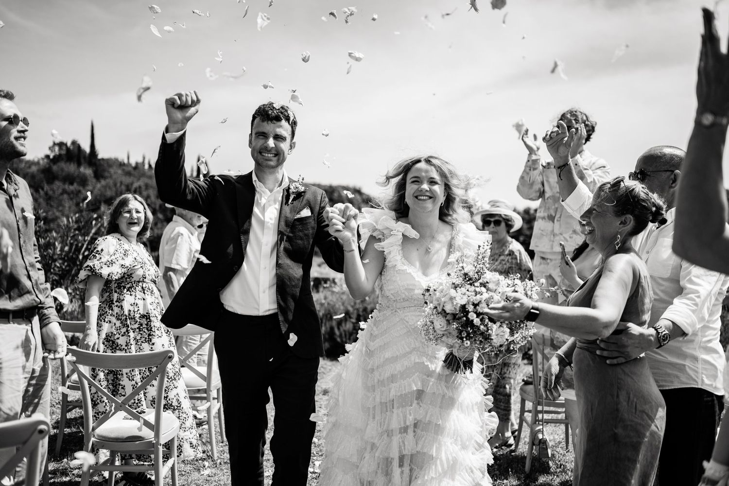 Black and white capture of joyful wedding celebration with confetti toss.