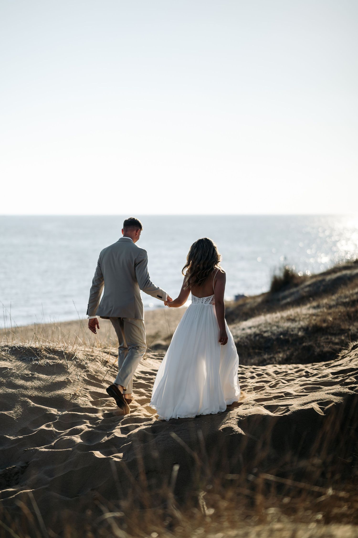 Newlyweds walk hand in hand along a coastal path with the ocean in the background.