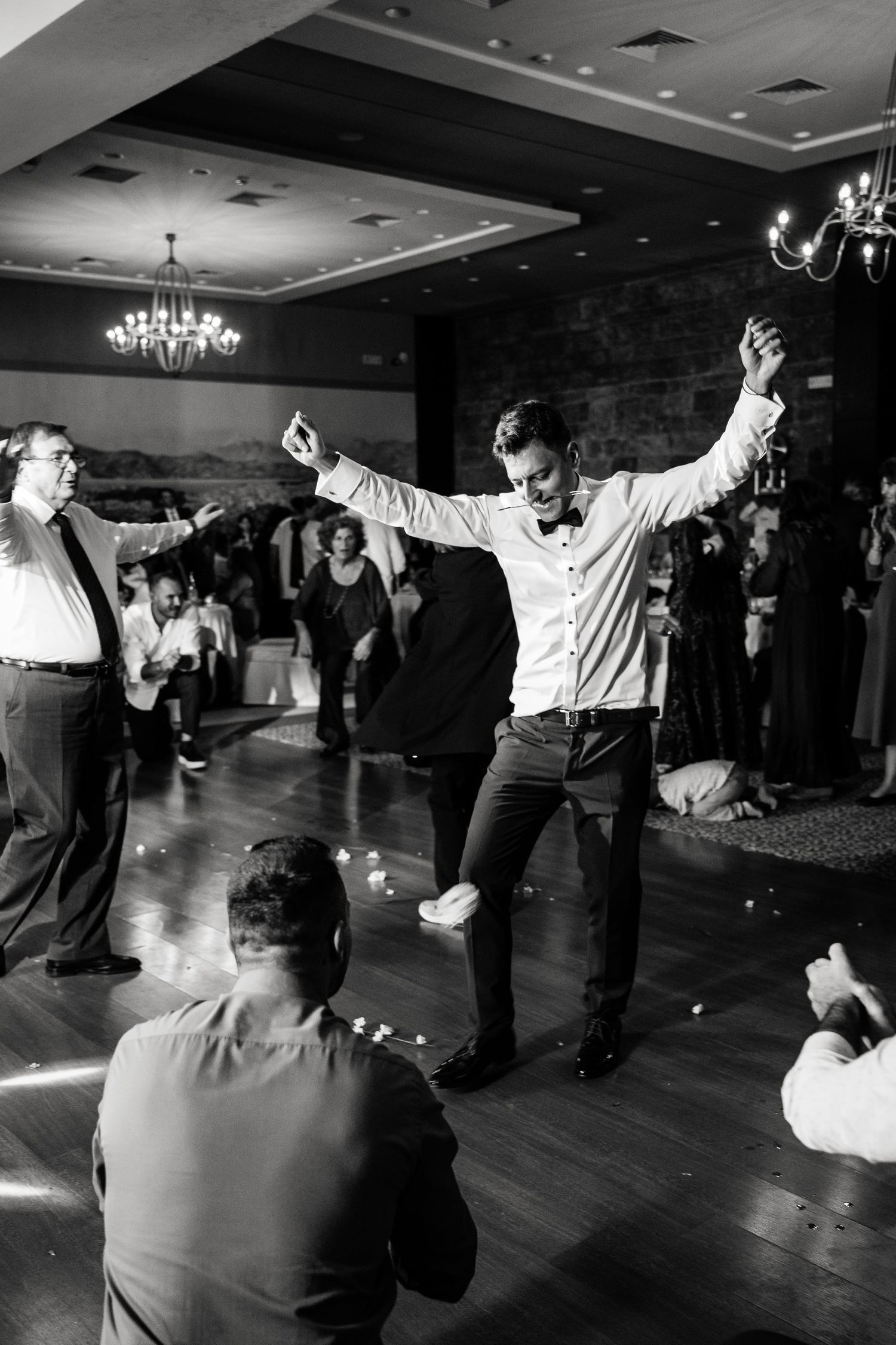 Black and white photo captures wedding guests dancing with raised arms in celebration.