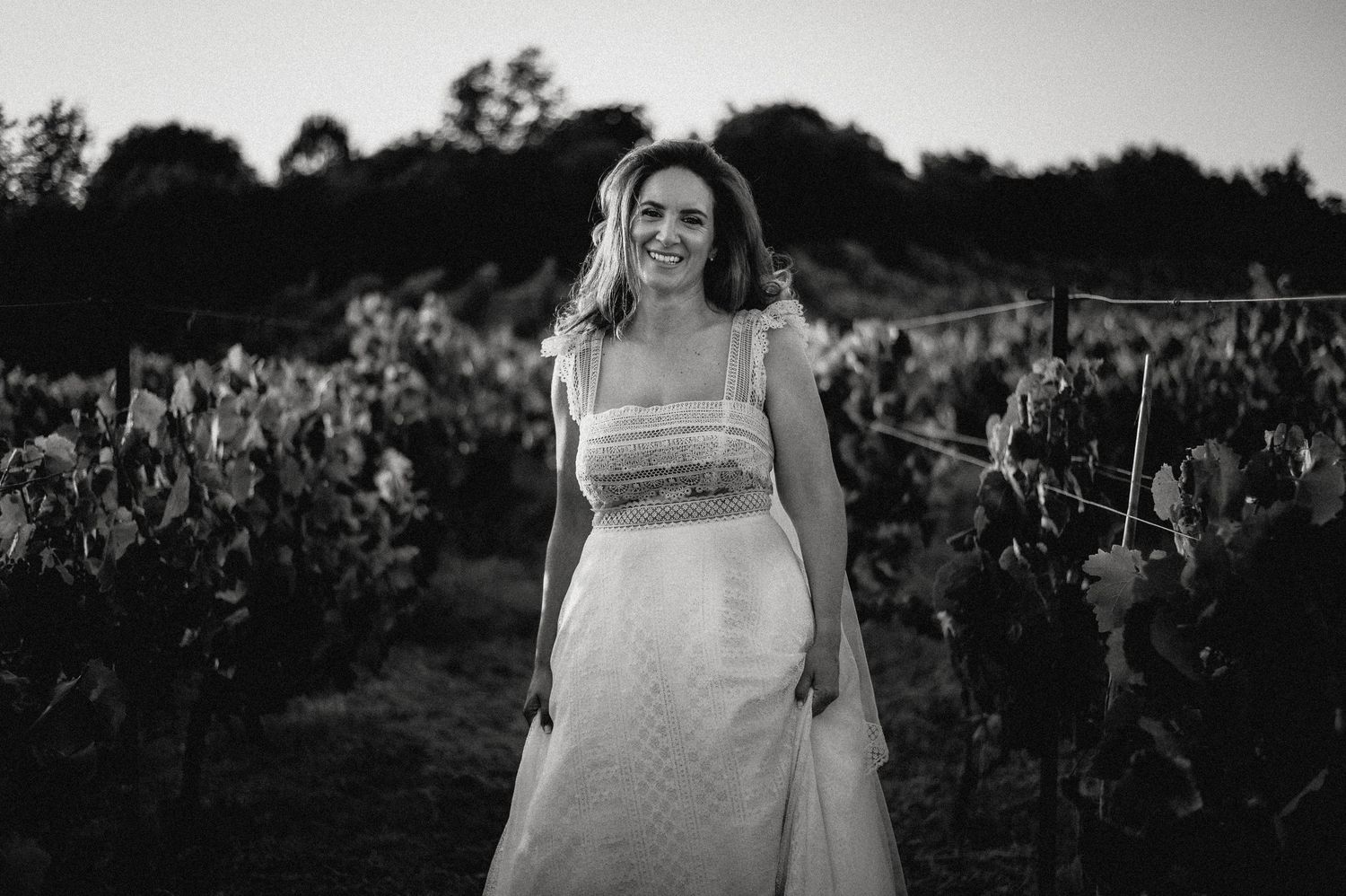 Bride poses in a white dress against a scenic vineyard backdrop.