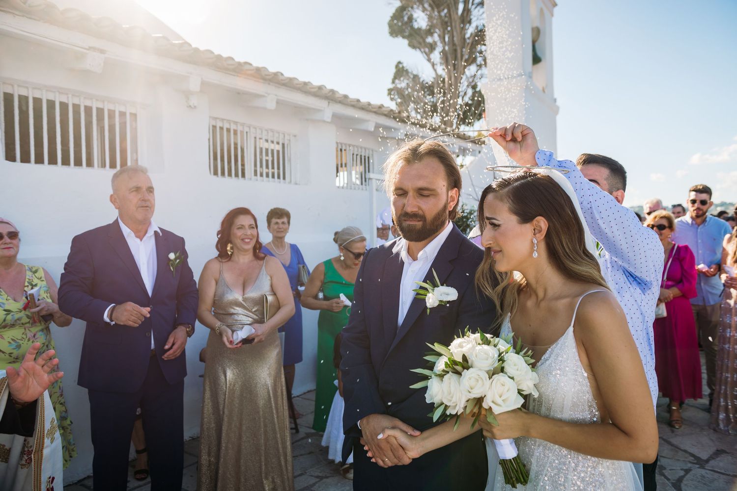 Wedding celebration with guests and white floral arrangements against white church architecture.