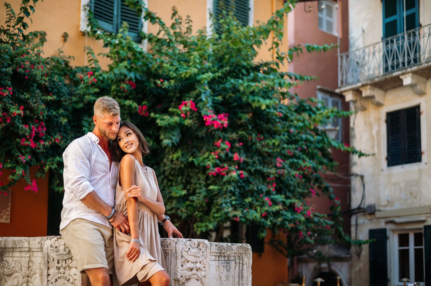 Couple sharing romantic moment among blooming bougainvillea and Mediterranean architecture.