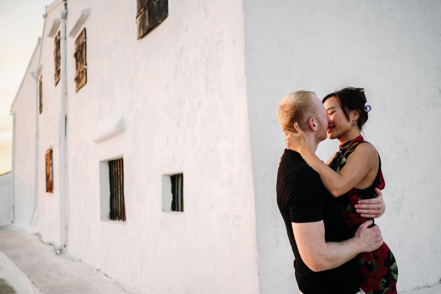 A couple embracing against a white Mediterranean building wall.