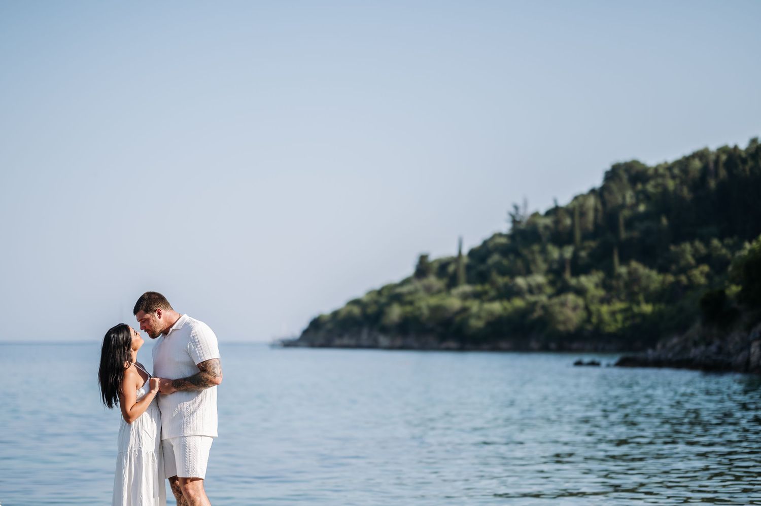 A tender moment between a couple in white outfits standing by the Mediterranean Sea.