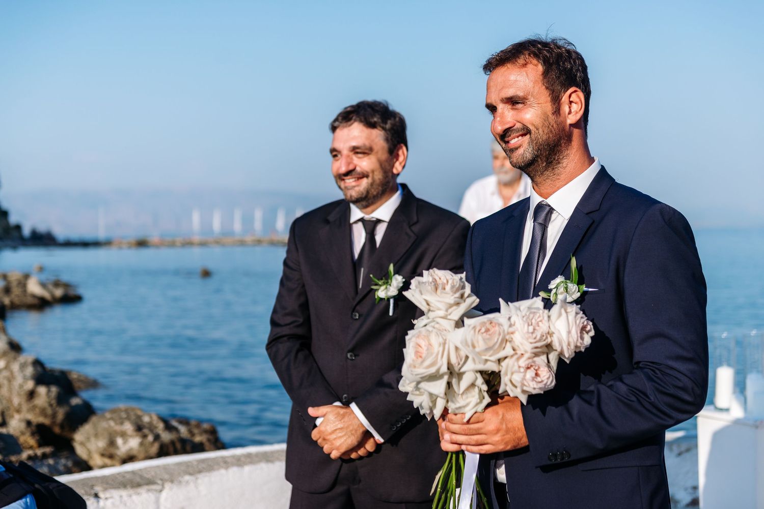 Groomsmen in navy suits share laughs during outdoor waterfront wedding photos.