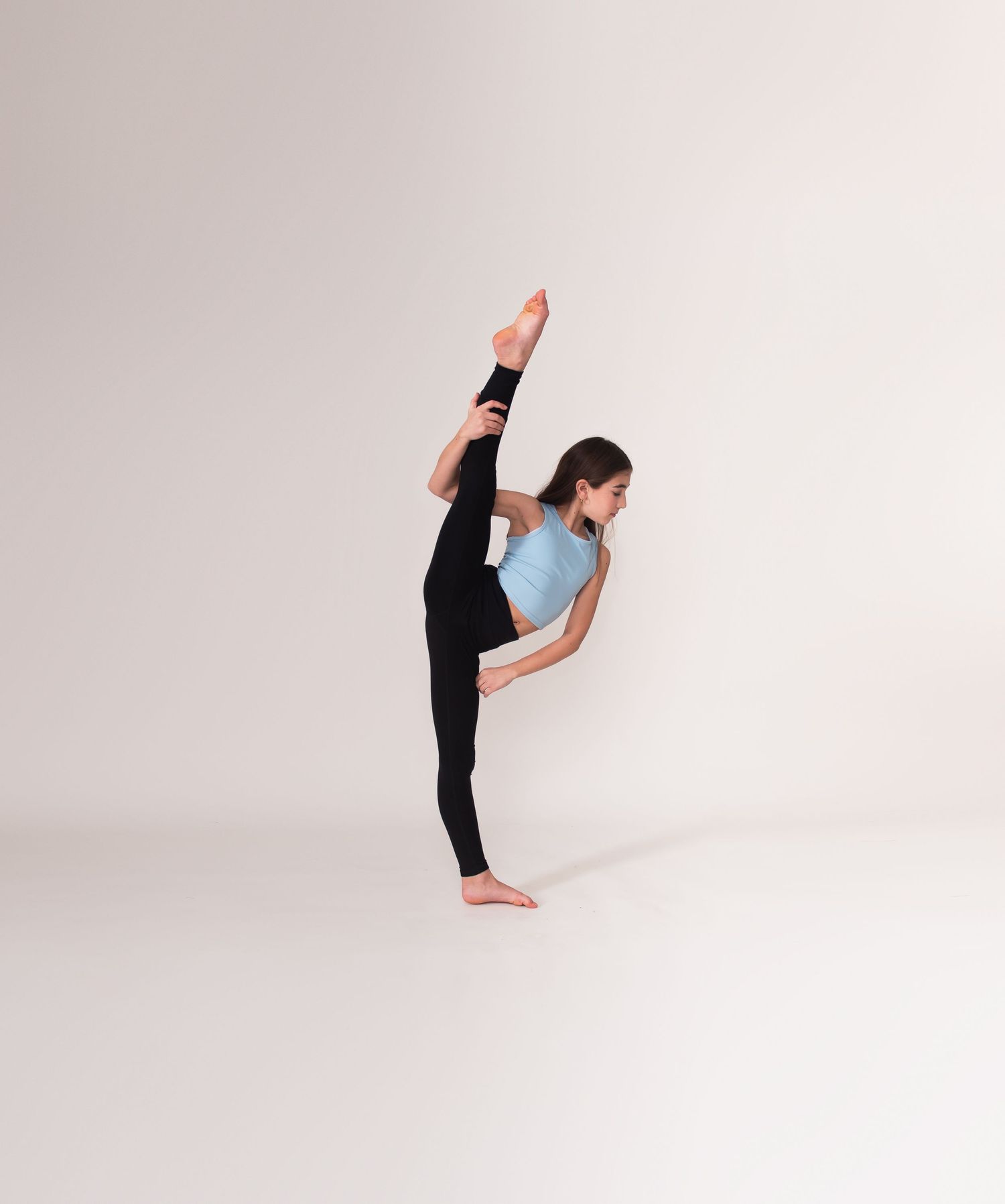 Athletic dancer performs standing split in blue crop top against white background.