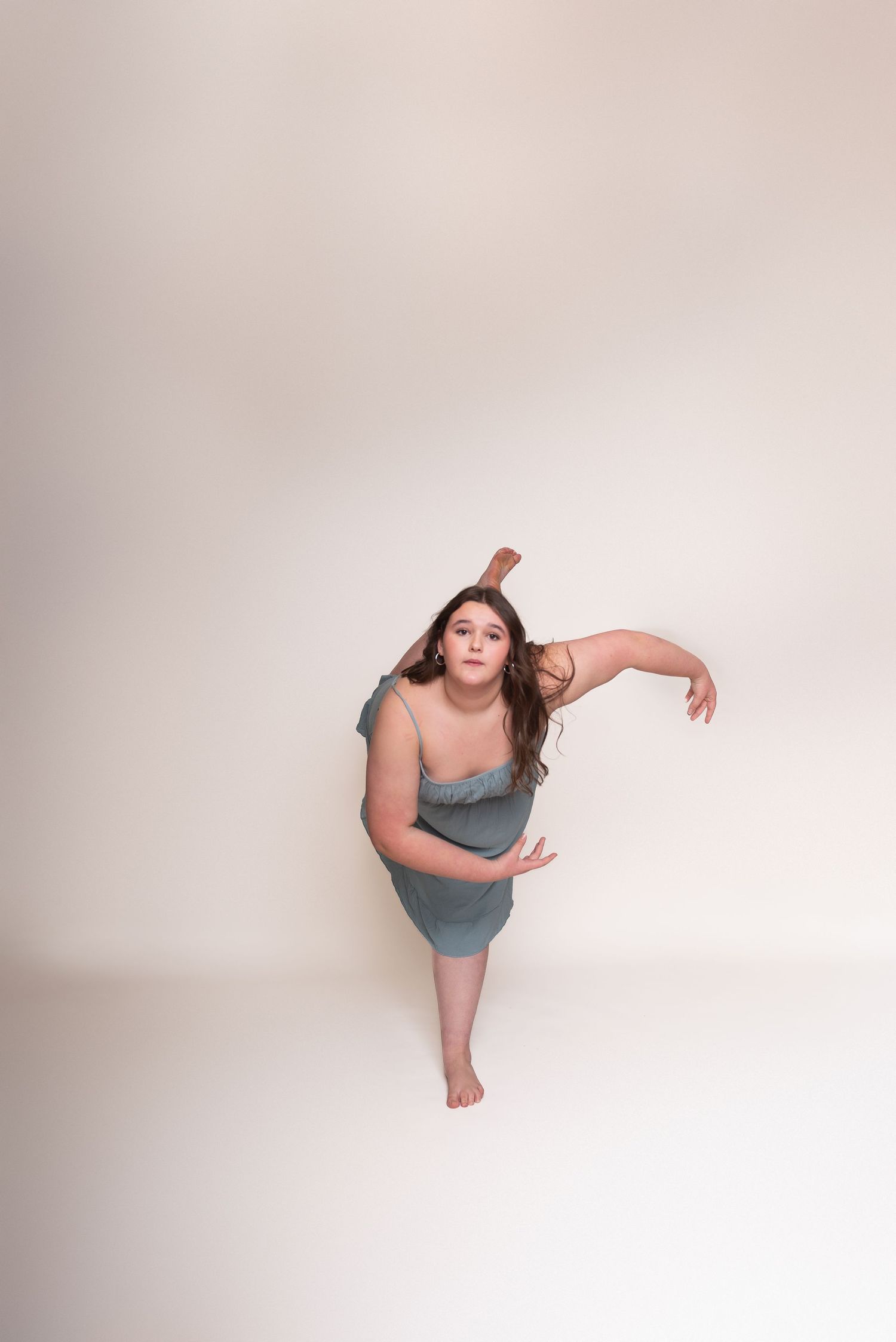 Dancer in blue dress performs expressive movements against a white studio background.