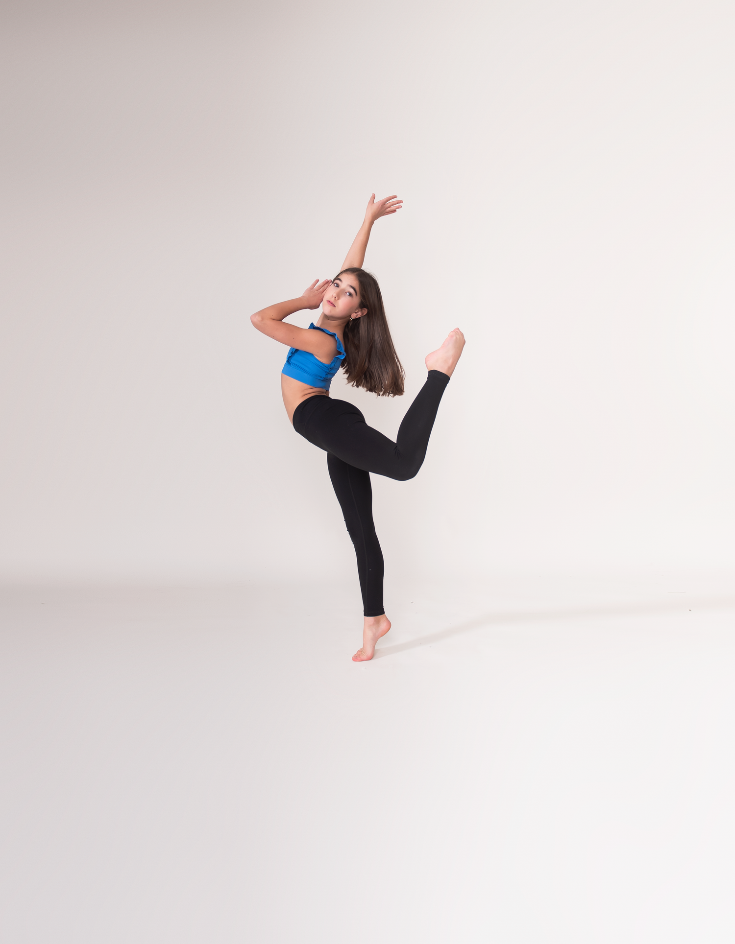 Dancer executes flowing movements in black outfit against minimalist white studio setting.