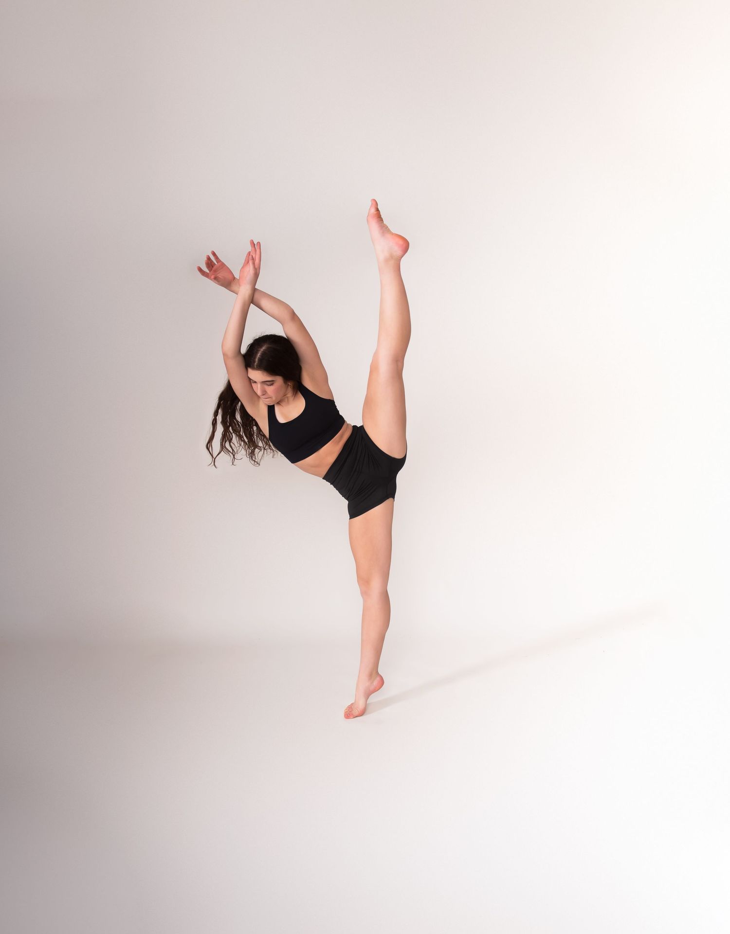 Dancer in black leotard performing graceful movements against white background.