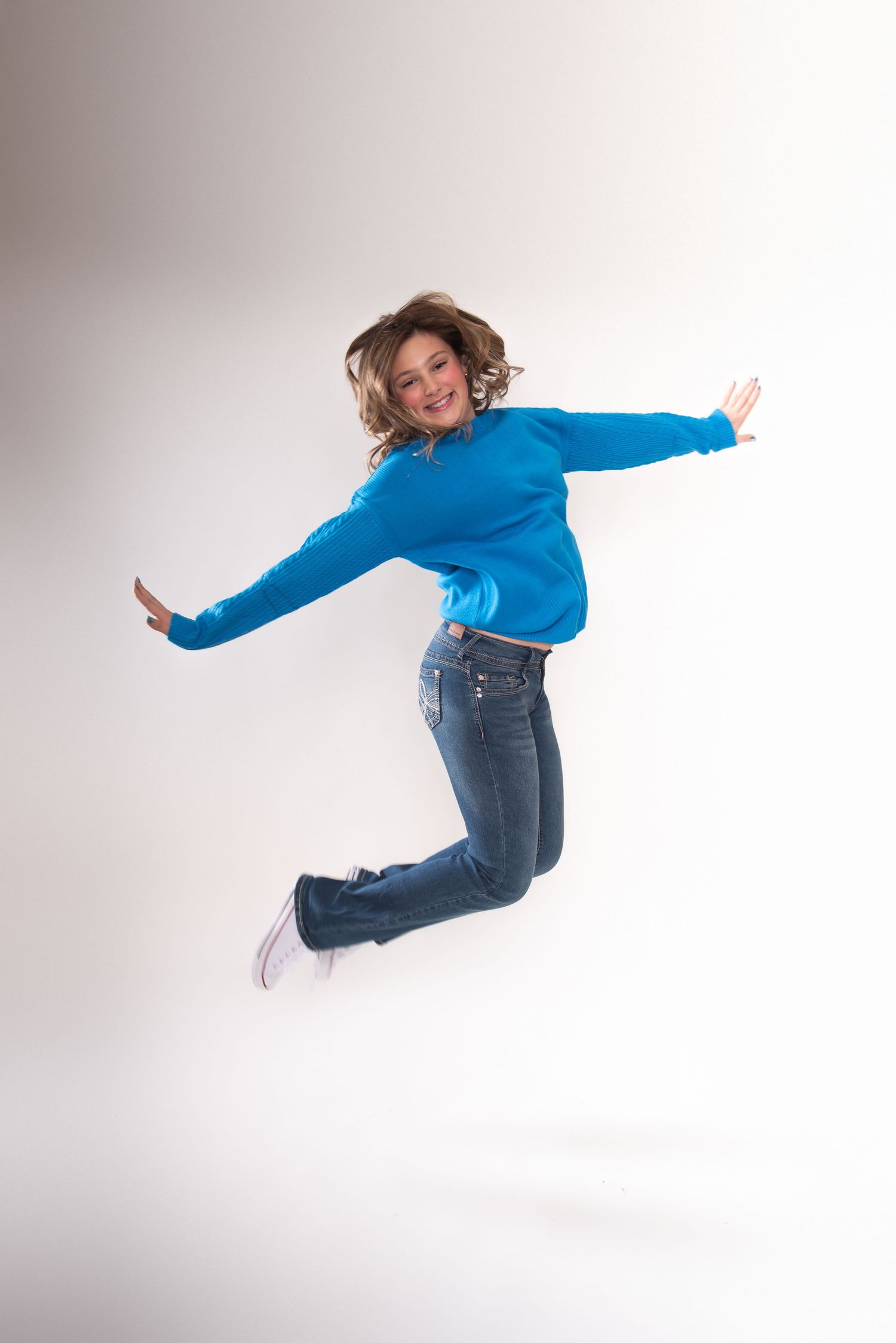 Person in blue sweater and jeans executes dynamic jump sequence against white backdrop.