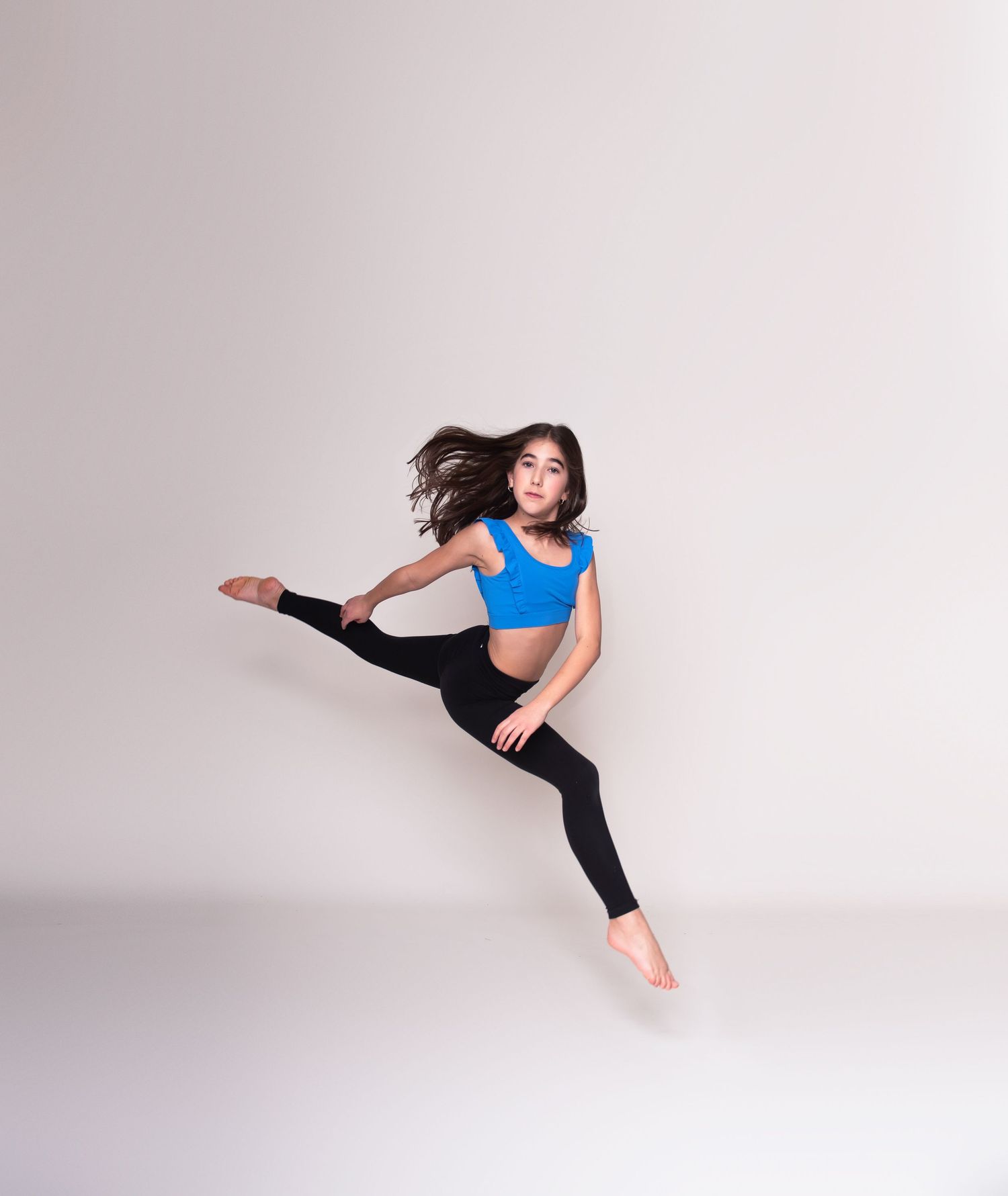 Dynamic dance leap captured against white studio background with flowing movement.
