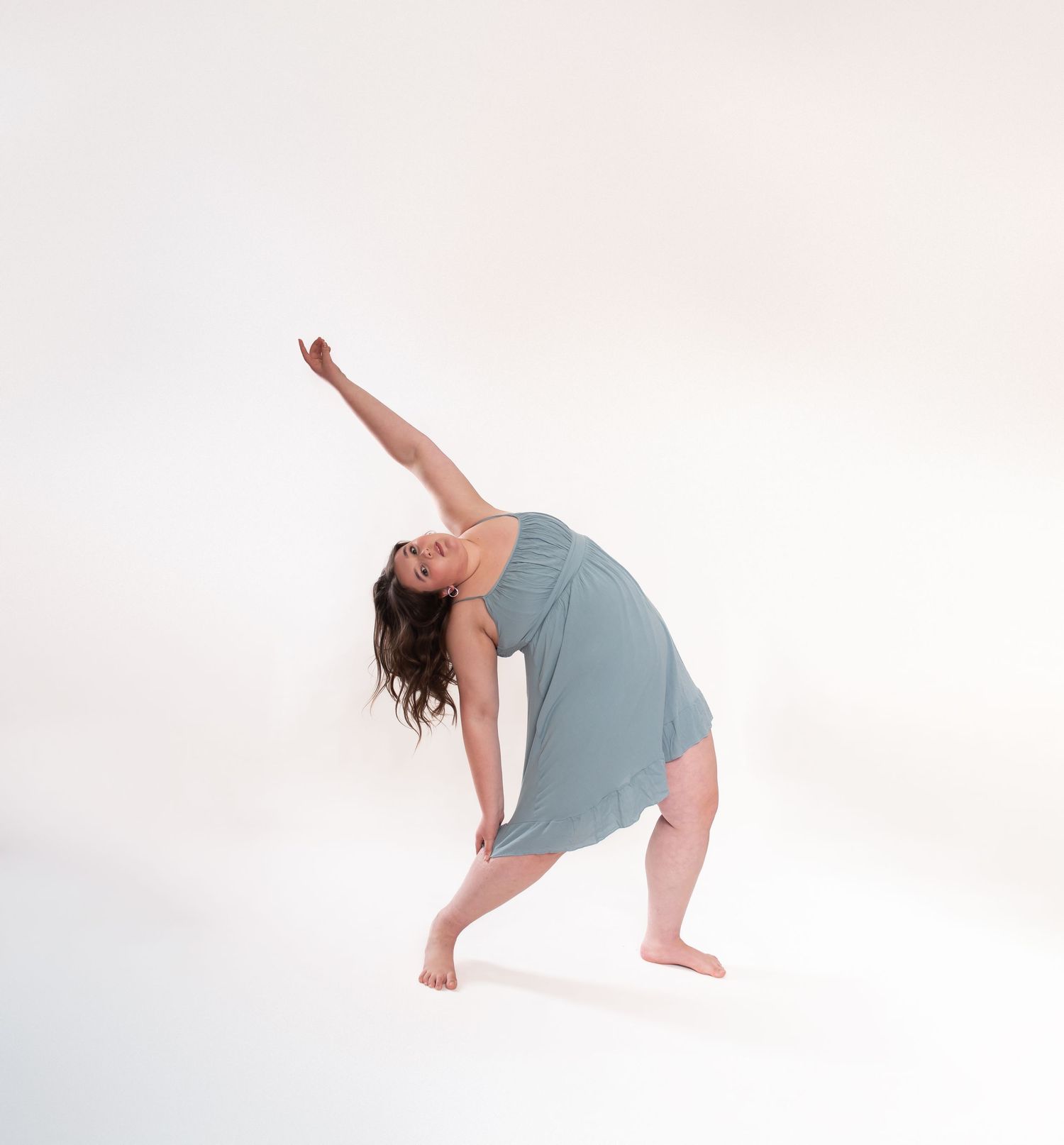 Dancer in grey clothing performs expressive modern dance movements in studio setting.