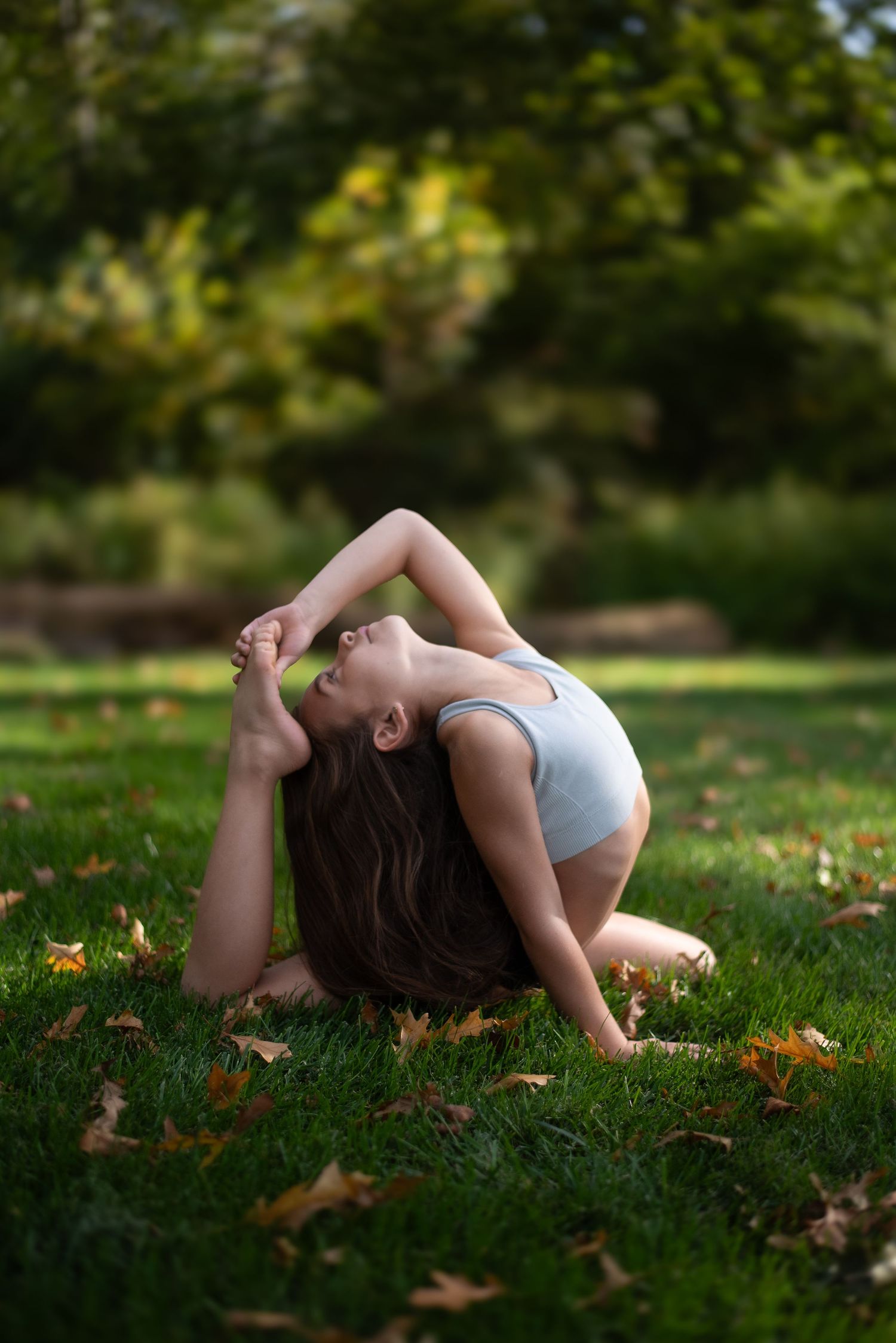 Dancer performs graceful backbend pose on grass with autumn leaves.