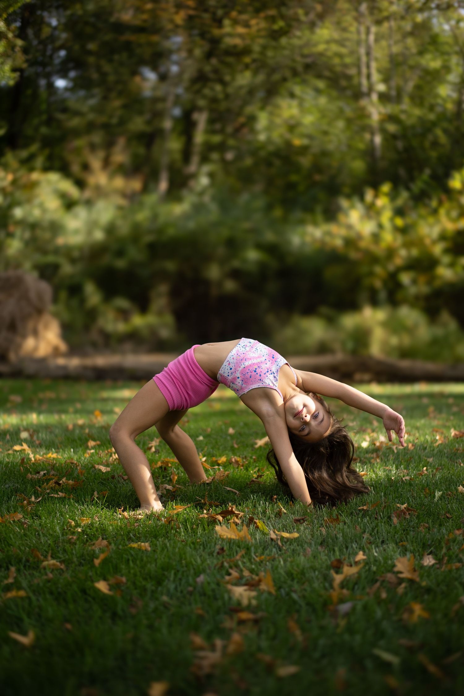 Graceful backbend pose performed on grass with autumn foliage in background.