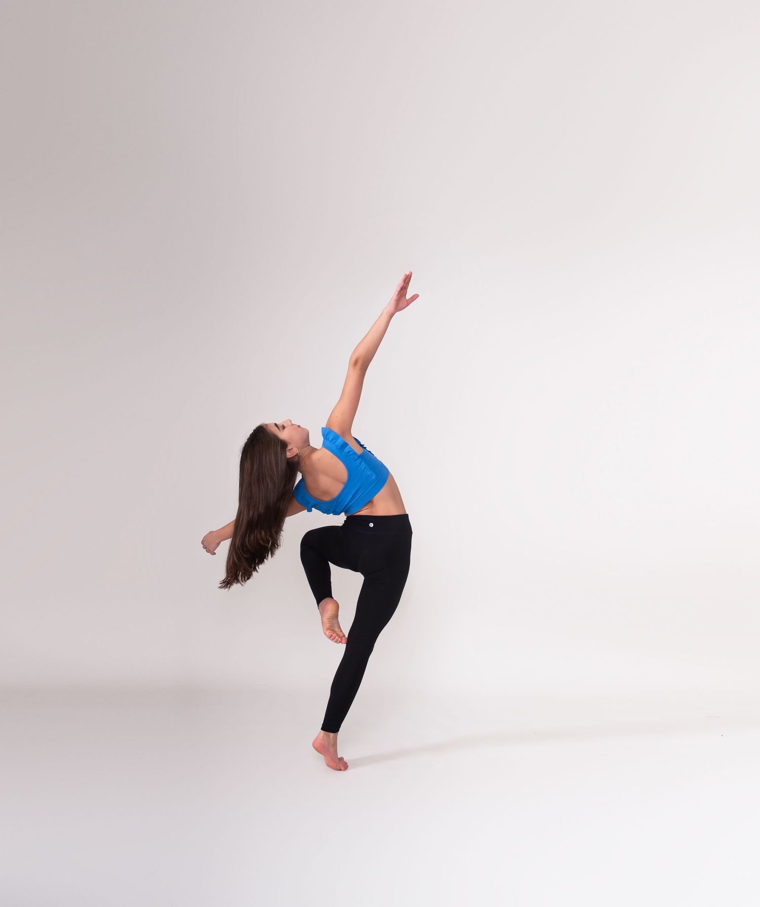 Dancer in blue top and black pants performs a graceful backbend pose against white background.