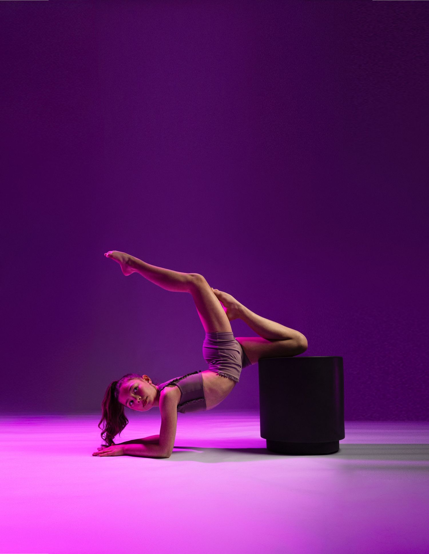 Flexible dancer balancing on a black cube under purple neon lights, performing an impressive acrobatic pose.
