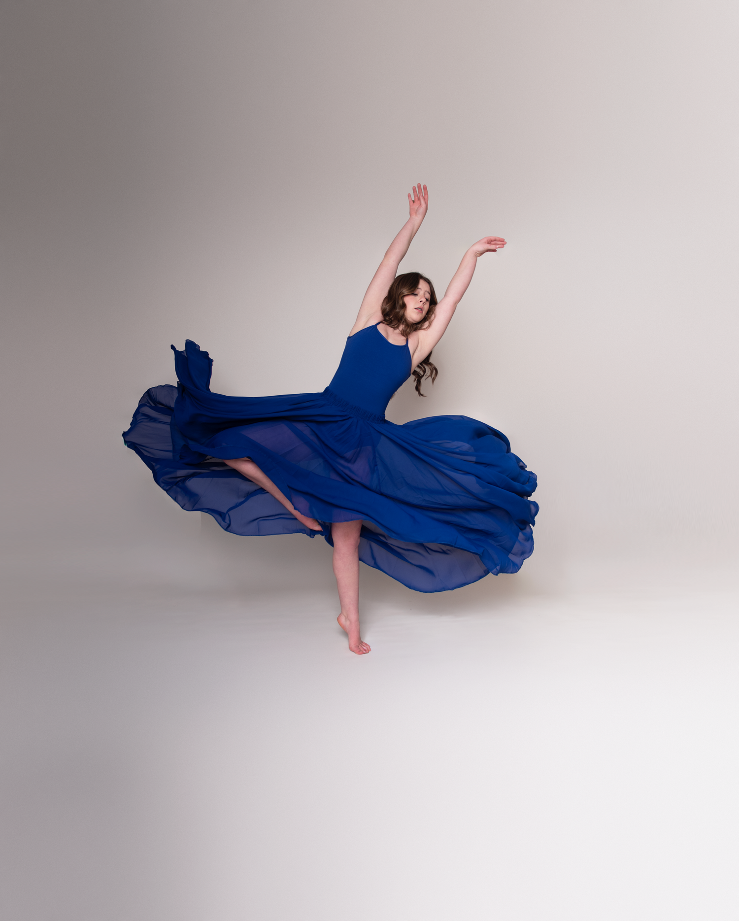 Dancer in flowing blue dress creates ethereal floating poses in studio setting.