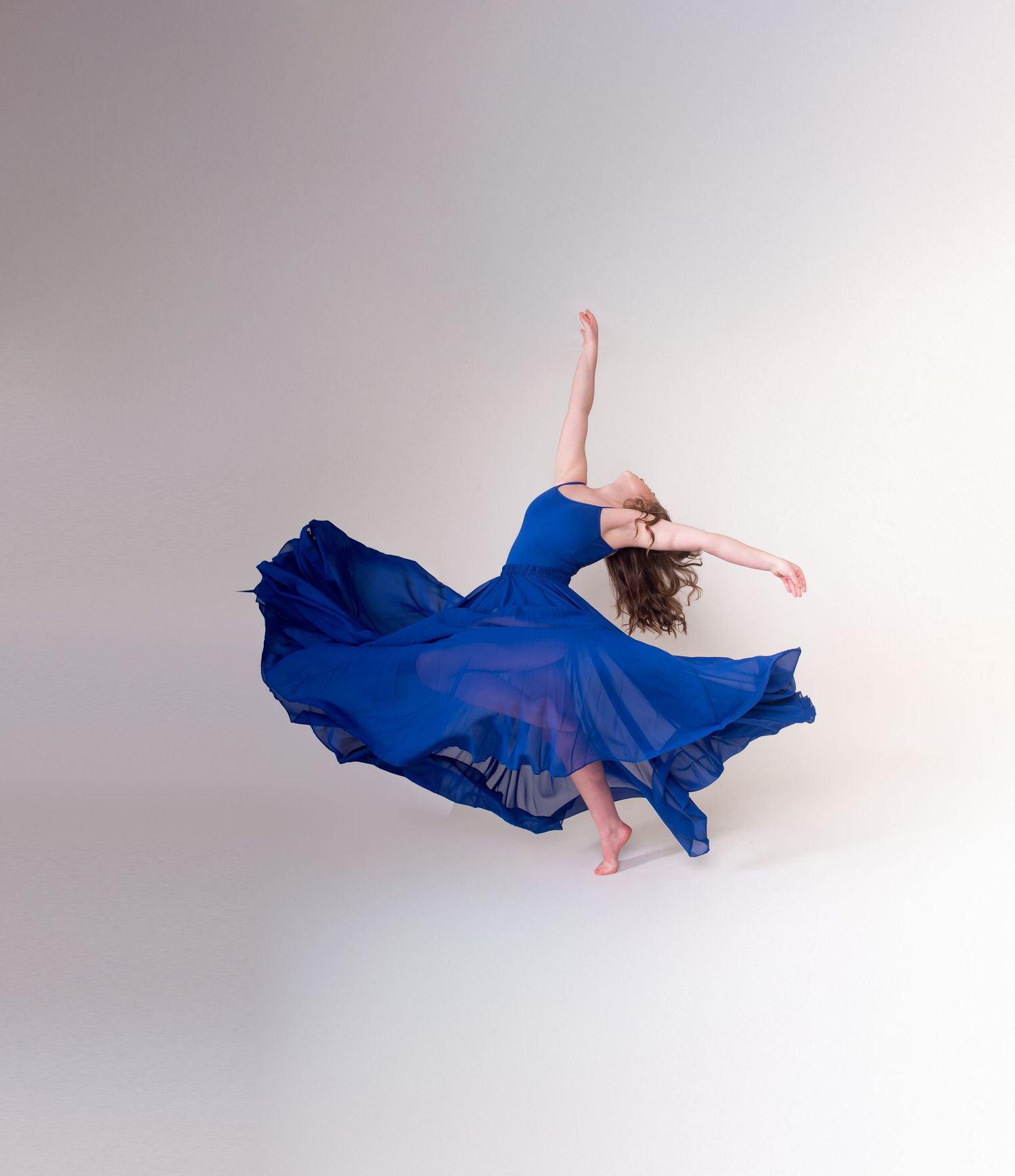 Graceful dance pose with billowing blue dress creating dramatic movement in studio setting.