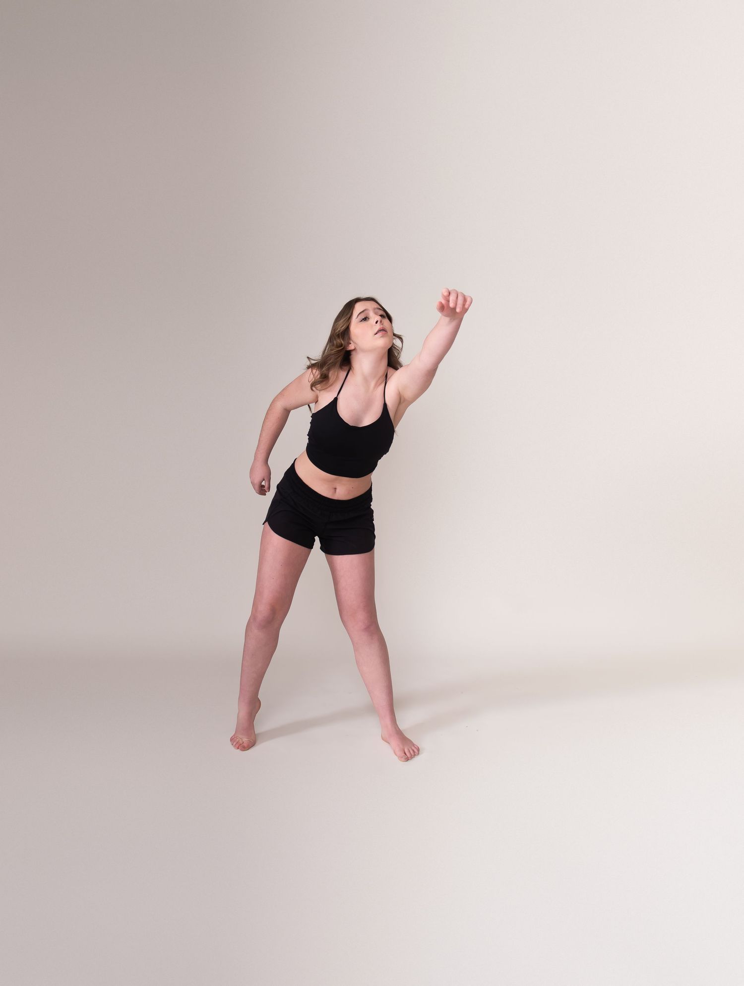 Dancer in black athletic wear strikes an expressive pose with upward reaching arms.