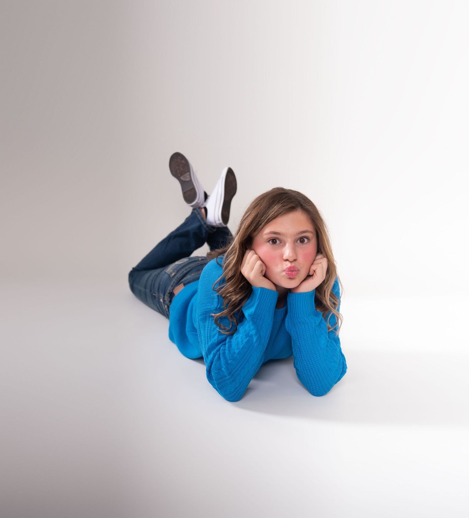 Person in bright blue outfit lying on floor in casual pose against white background.