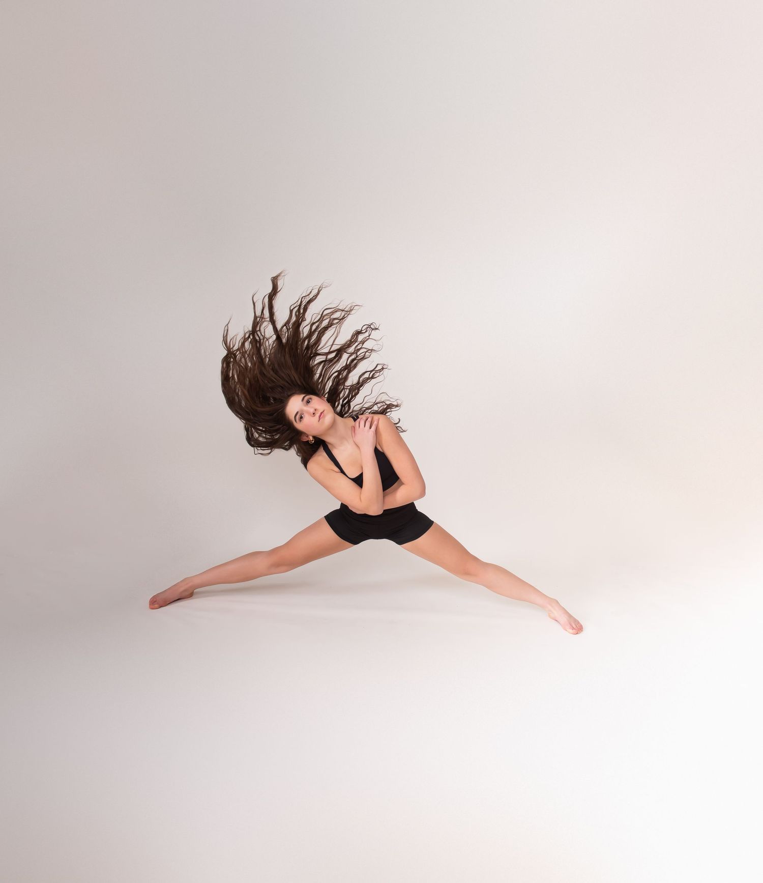 Dancer performs a graceful leap sequence in black attire against a white studio backdrop.