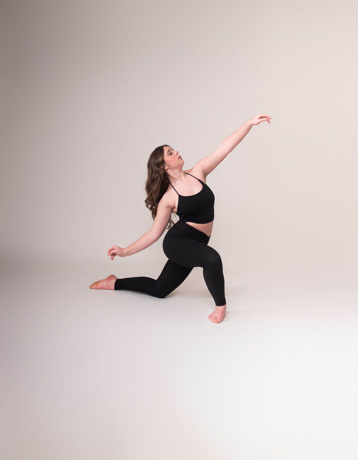 Modern dancer performs fluid movements in black attire against minimalist white backdrop.