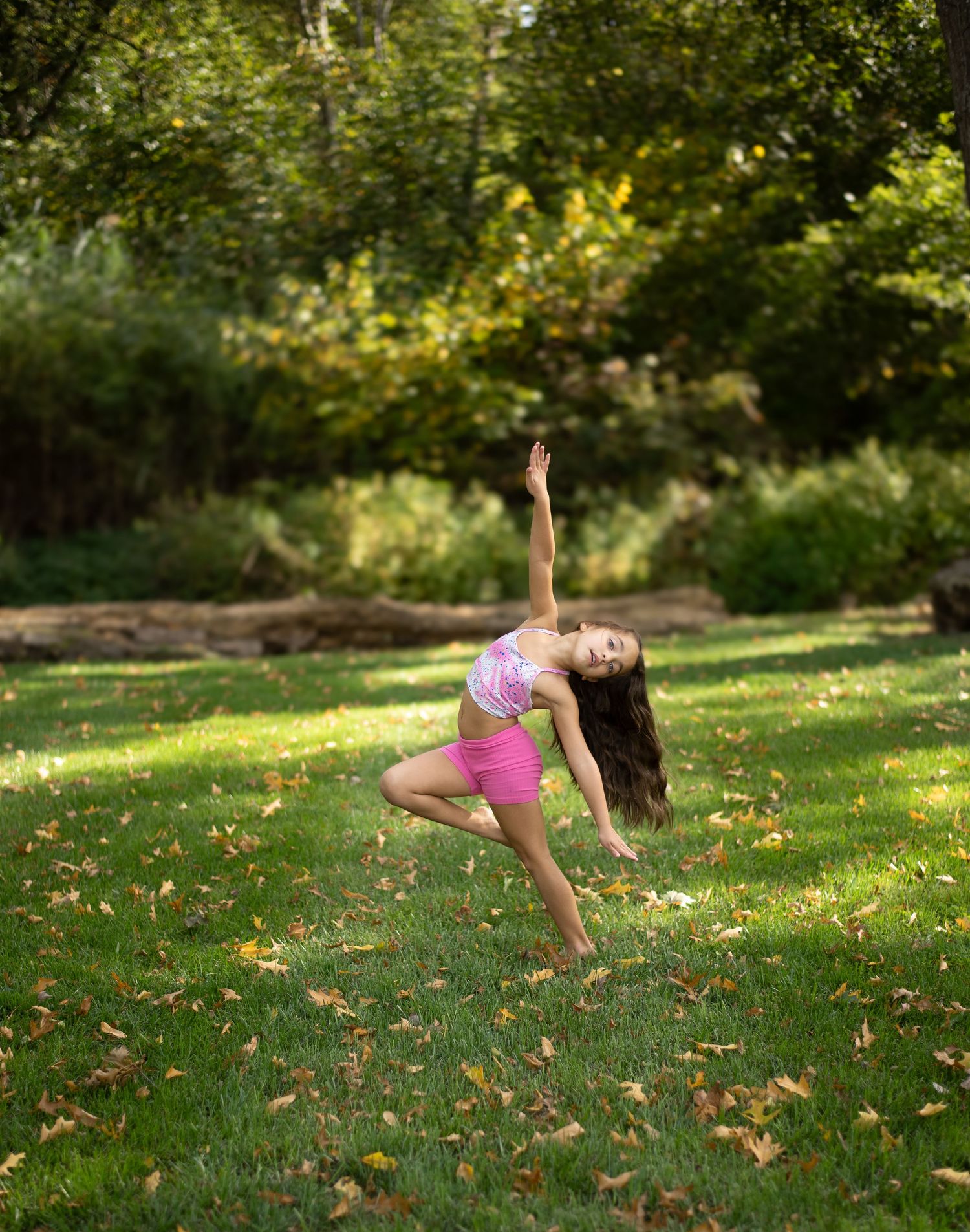 Dancer performing expressive movements outdoors on grass with autumn leaves.