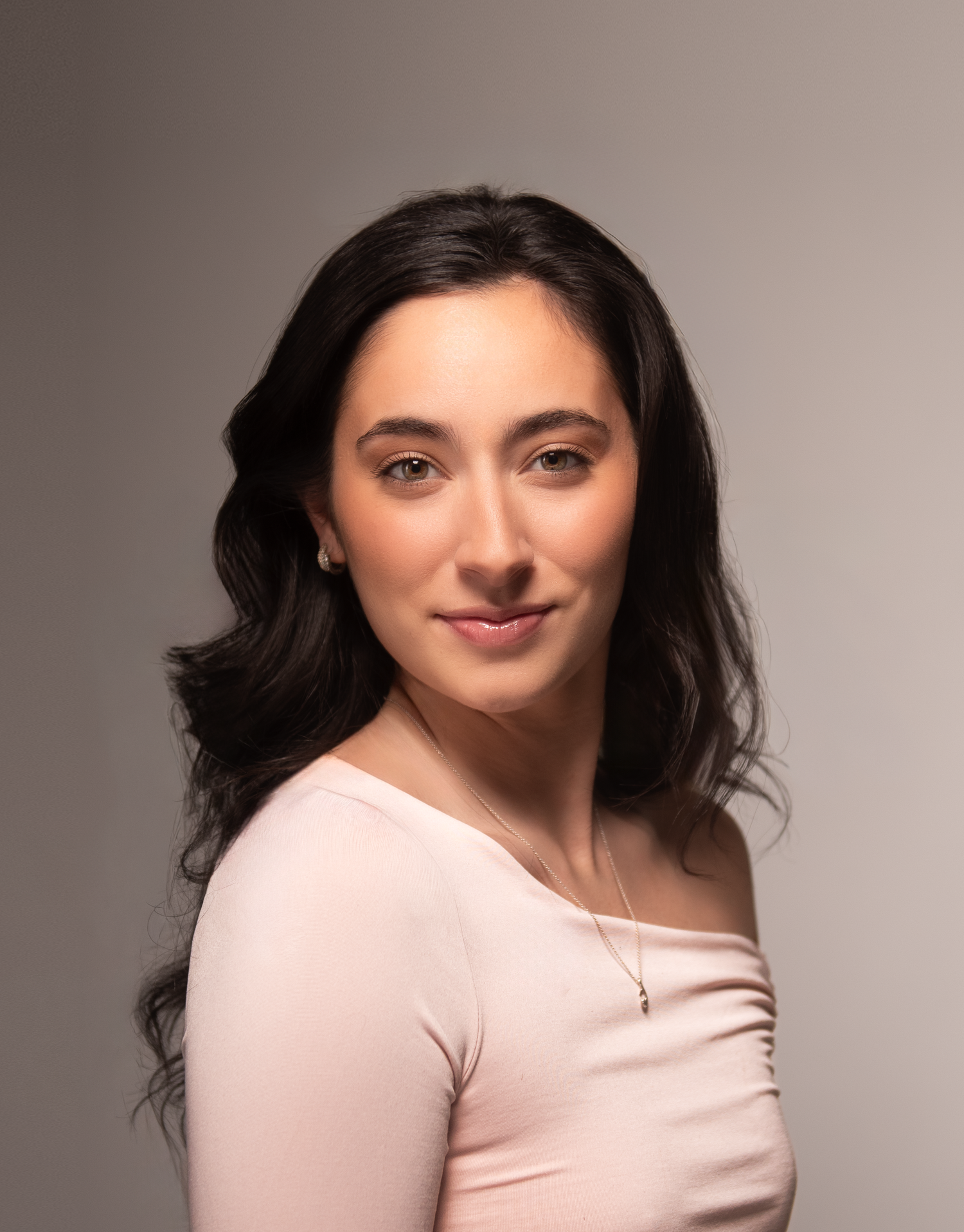 Studio portrait of a dancer wearing pink off-shoulder top against neutral background.