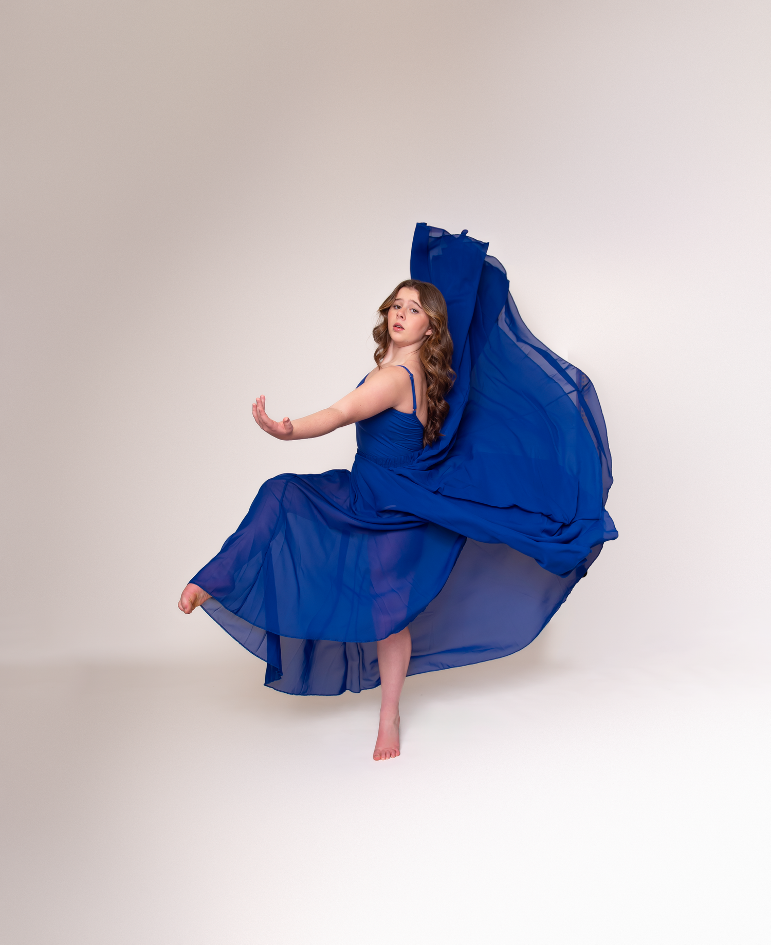 Dancer in flowing royal blue dress creates elegant movement sequence against white backdrop.