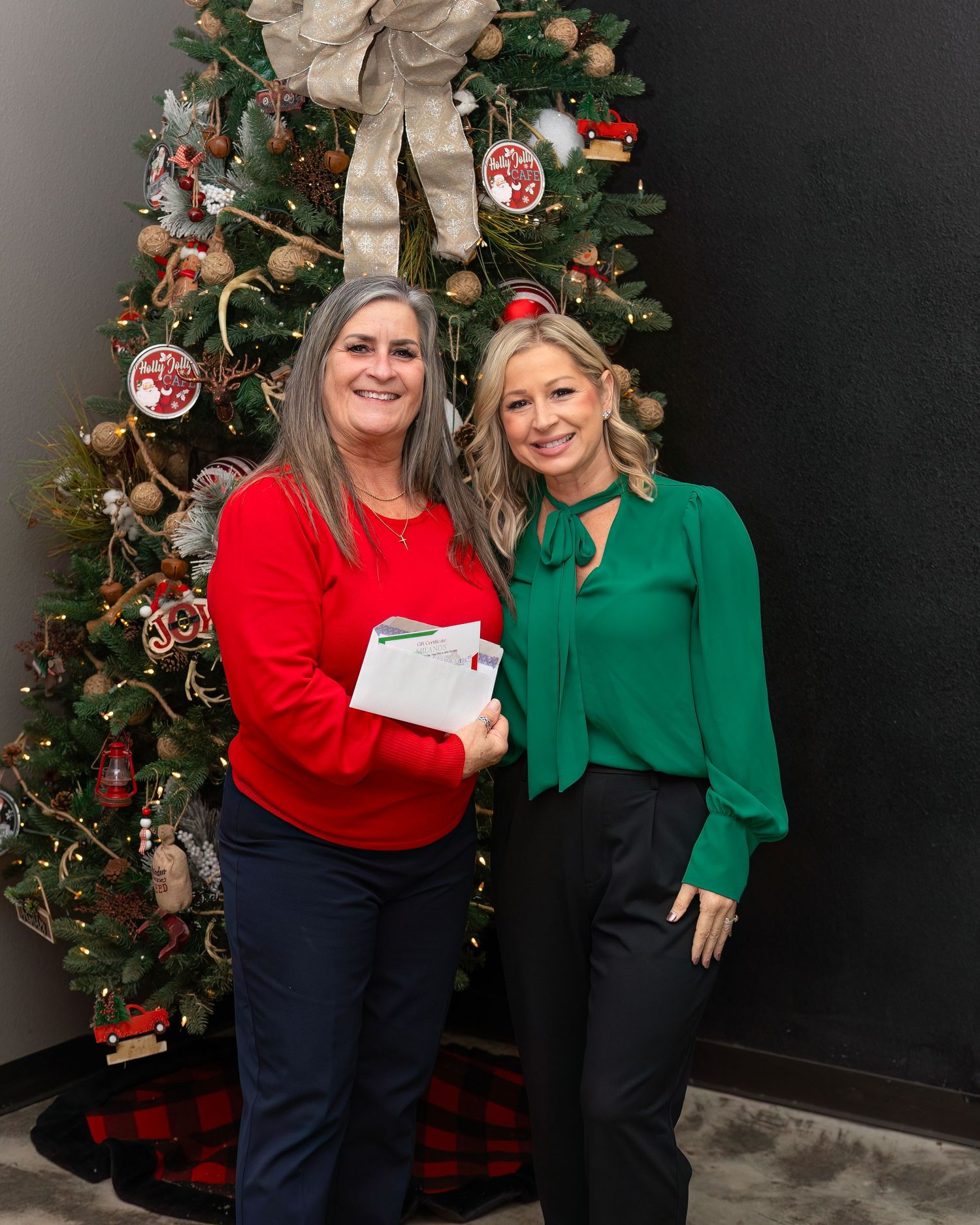 Bridge City Chamber of Commerce with two people in red and green holiday outfits pose together in front of a decorated Christmas tree.