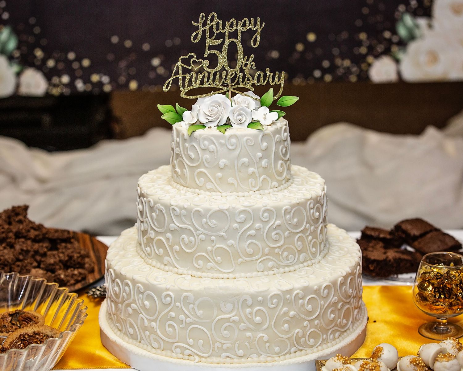 50th Wedding Anniversary with white wedding cake with delicate swirl patterns and floral decorations displayed at a reception table.