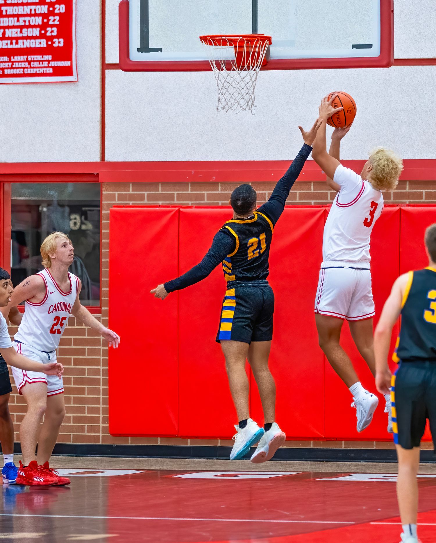 Basketball Game with players leaping g high during an intense game on a court with red walls and white markings.