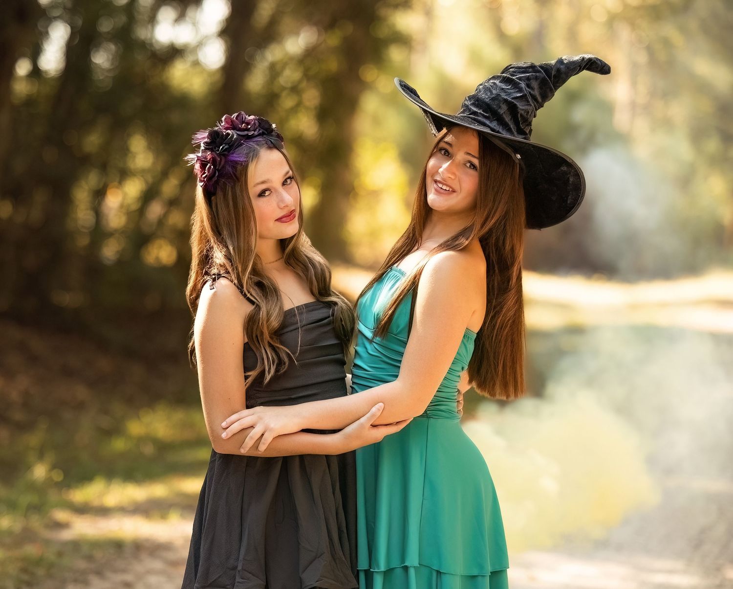 Two people in coordinating green and black dresses share a laugh while walking outdoors in golden sunlight.